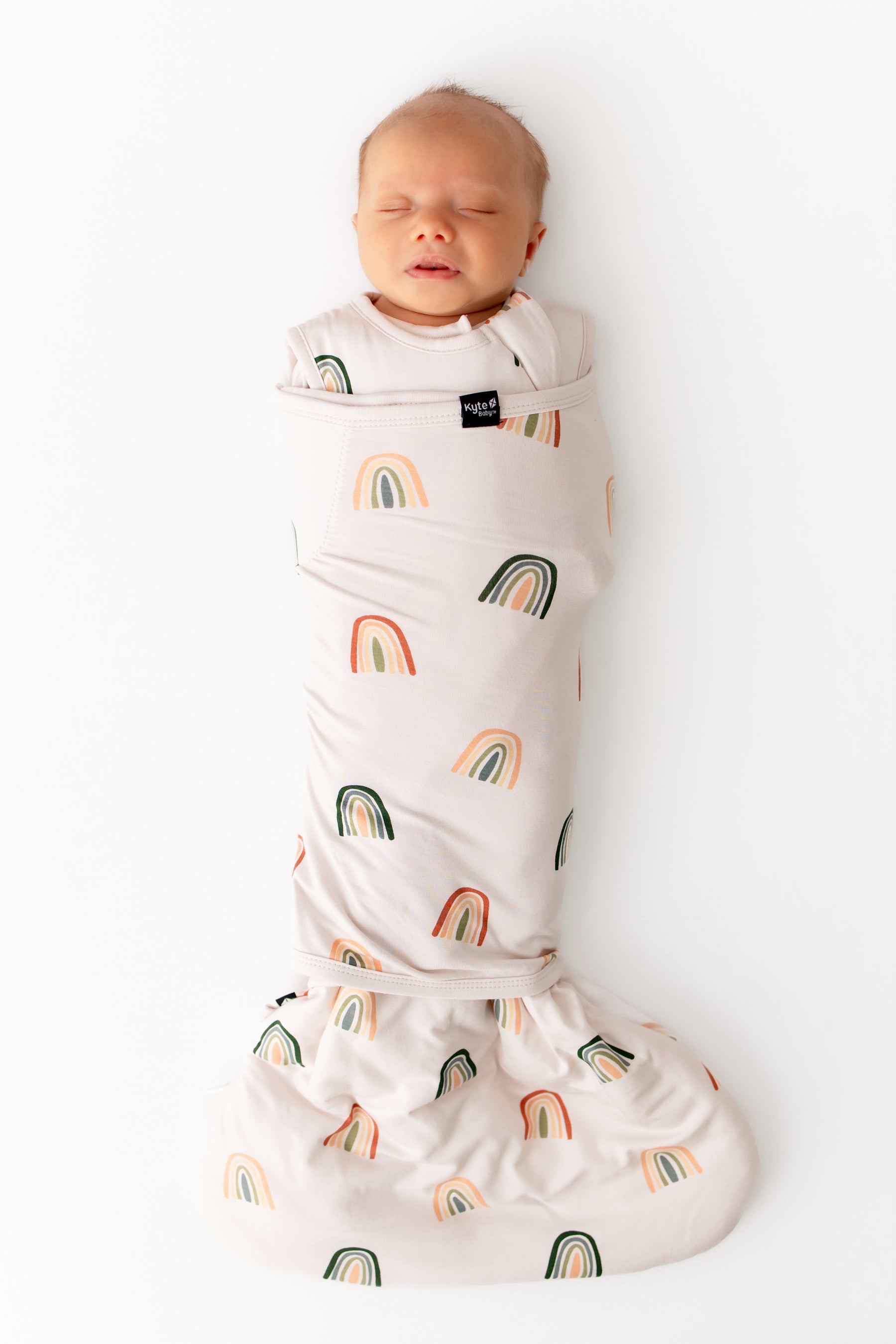 Baby sleeping in Sleep Bag Swaddler in Retro Rainbow 1.0 print on a white background
