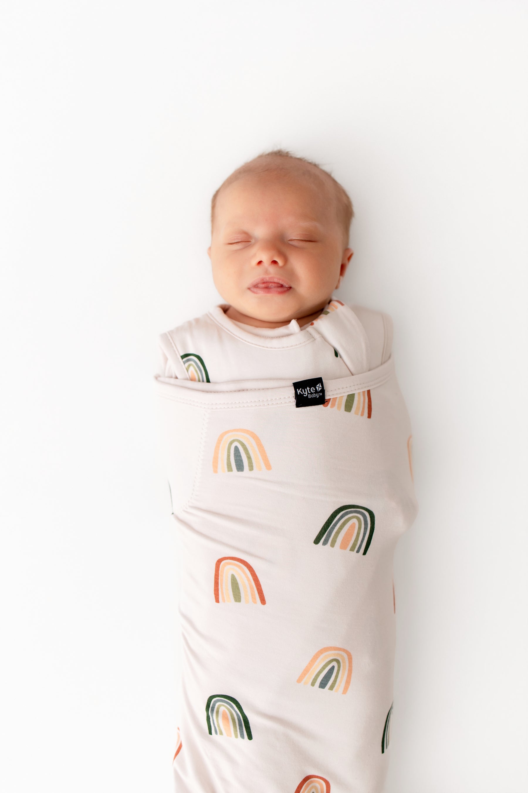 Baby sleeping in Sleep Bag Swaddler in Retro Rainbow 1.0 print on a white background