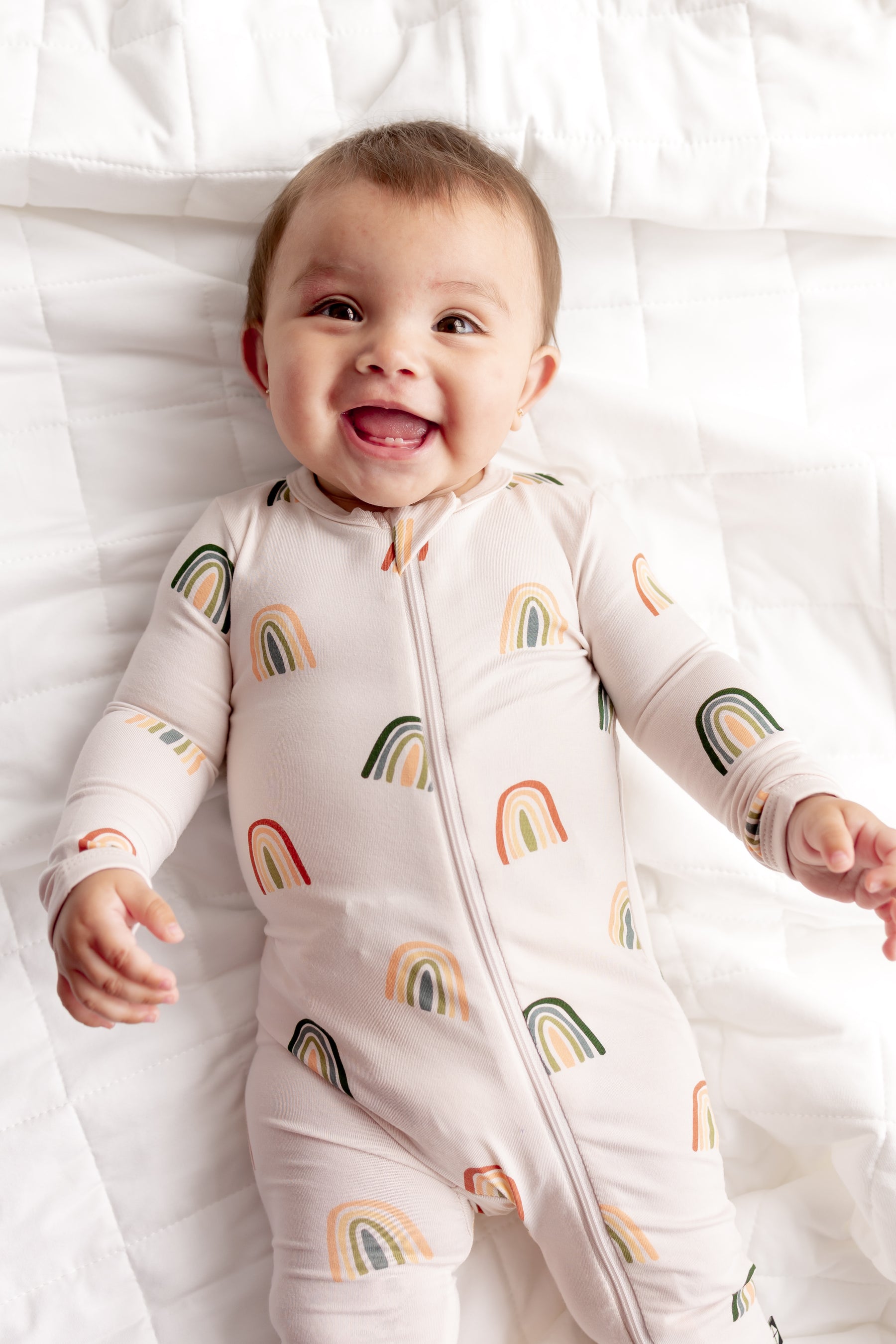 Baby smiling in Zippered Romper in Retro Rainbow print on a white sheet
