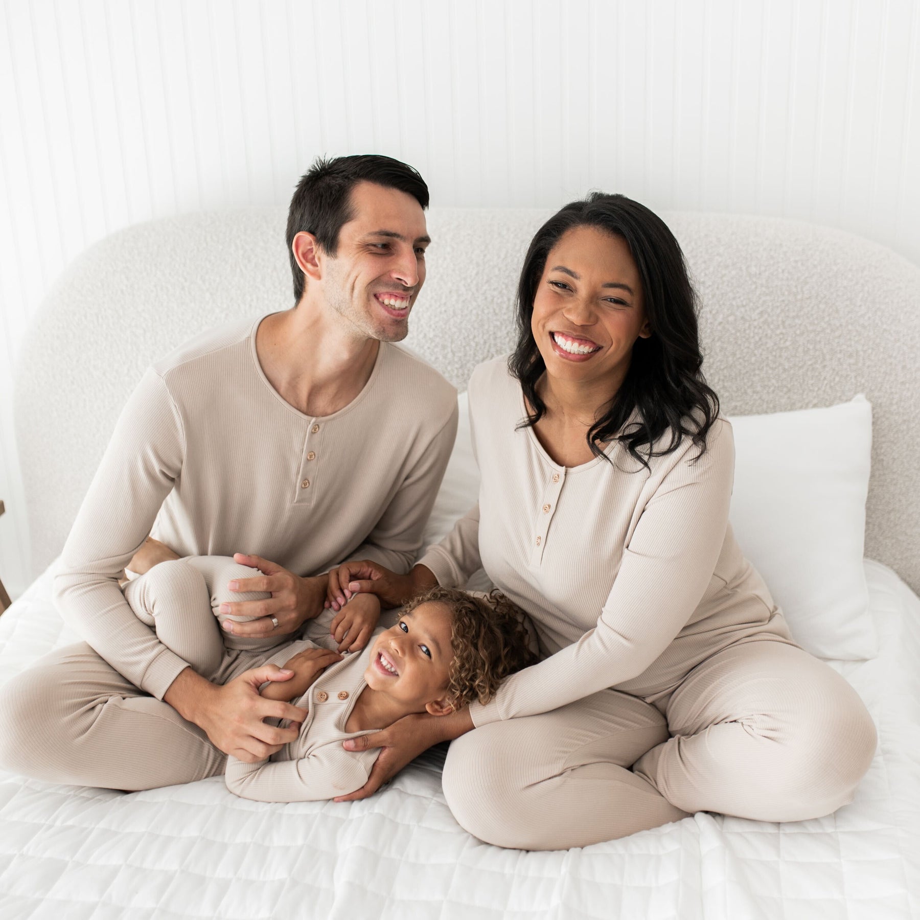 Family of three sitting on a bed wearing matching pajamas.