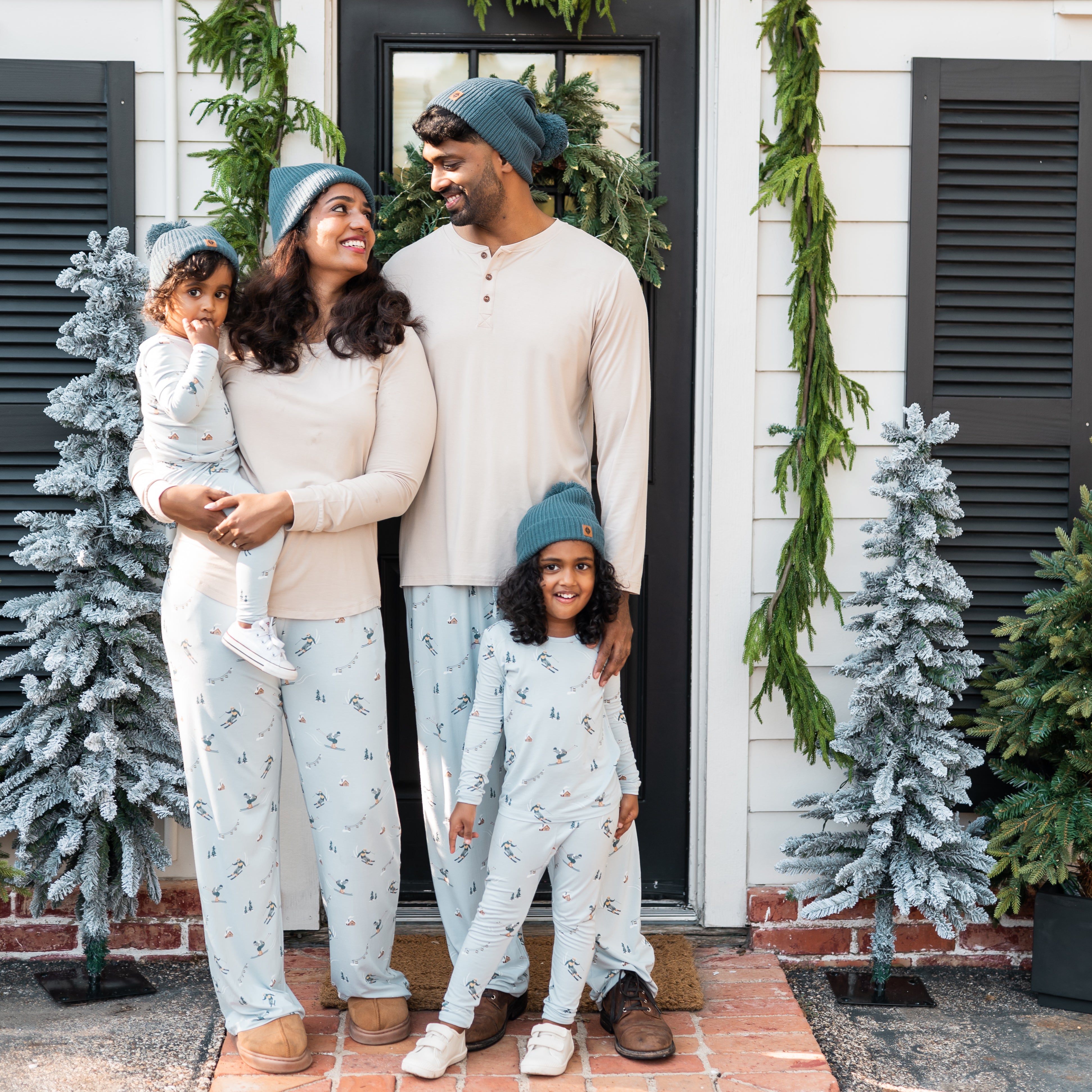 Family of four matching in ski items standing in front of a front door of a house
