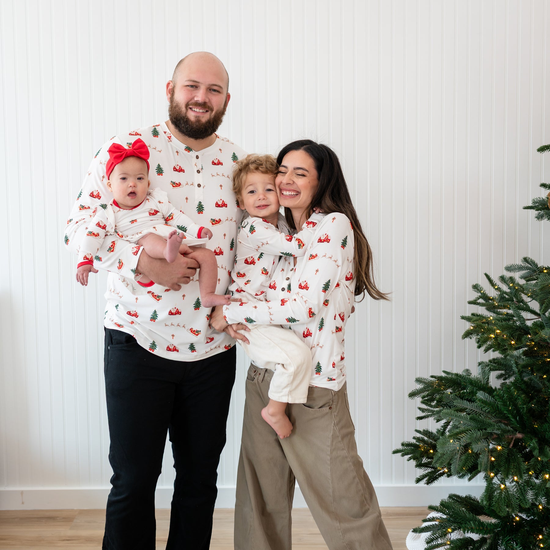 Family of four matching in Santa Sleigh. Pictured are the Long Sleeve Twirl Bodysuit Dress in Santa Sleigh, Men's, Women's and Toddler Henley tops