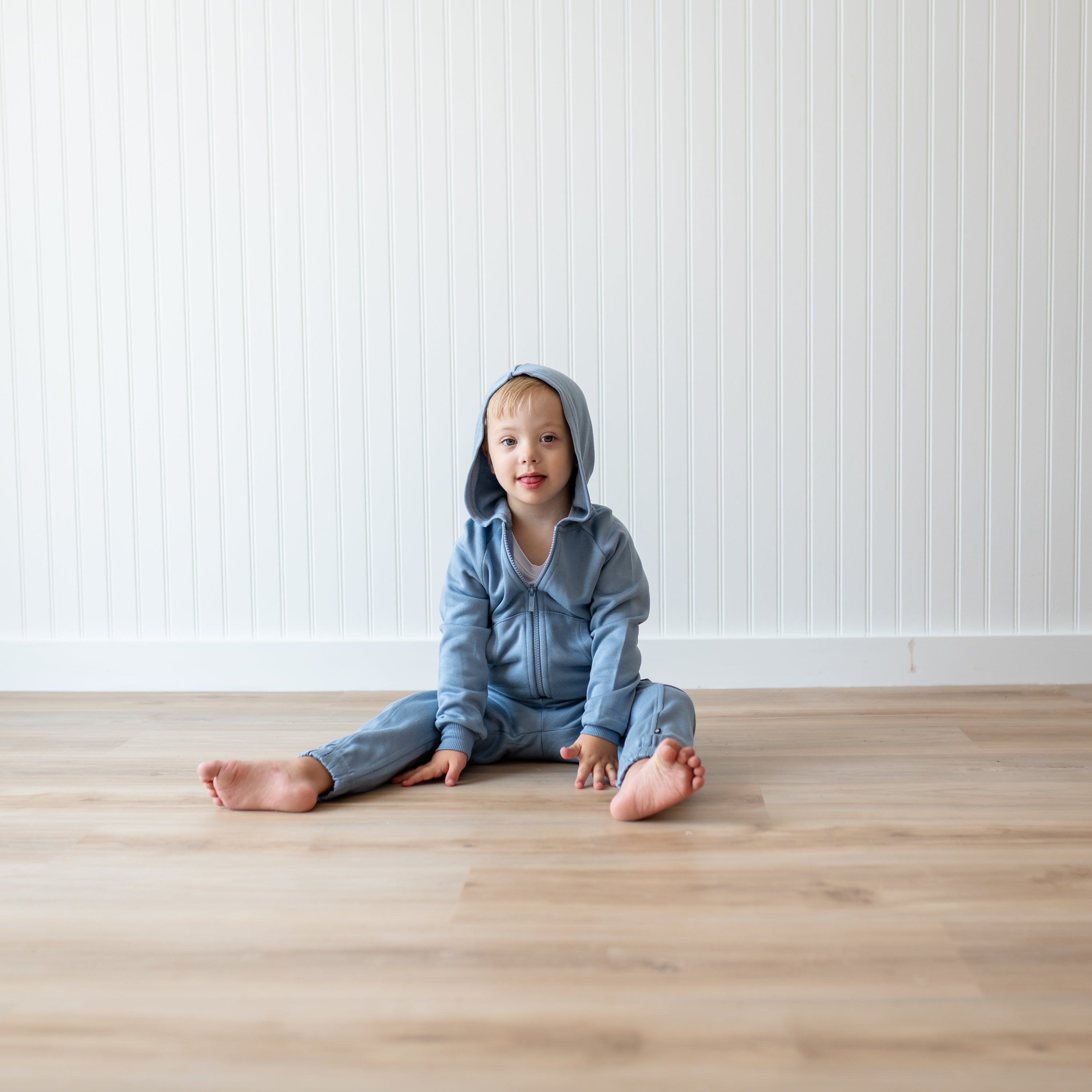 Young boy sitting on the floor in front of a white paneled wall wearing the Fleece Cargo Pants in Slate and matching fleece zip hoodie