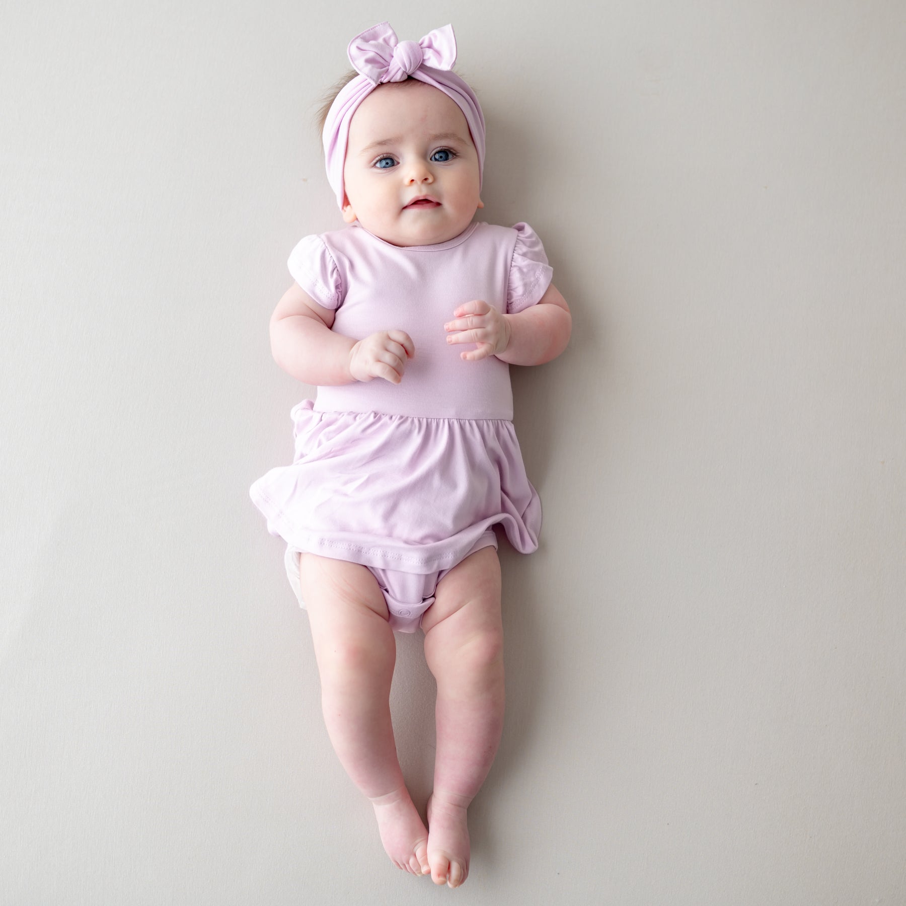 Baby in a purple outfit with a matching headband on a plain background