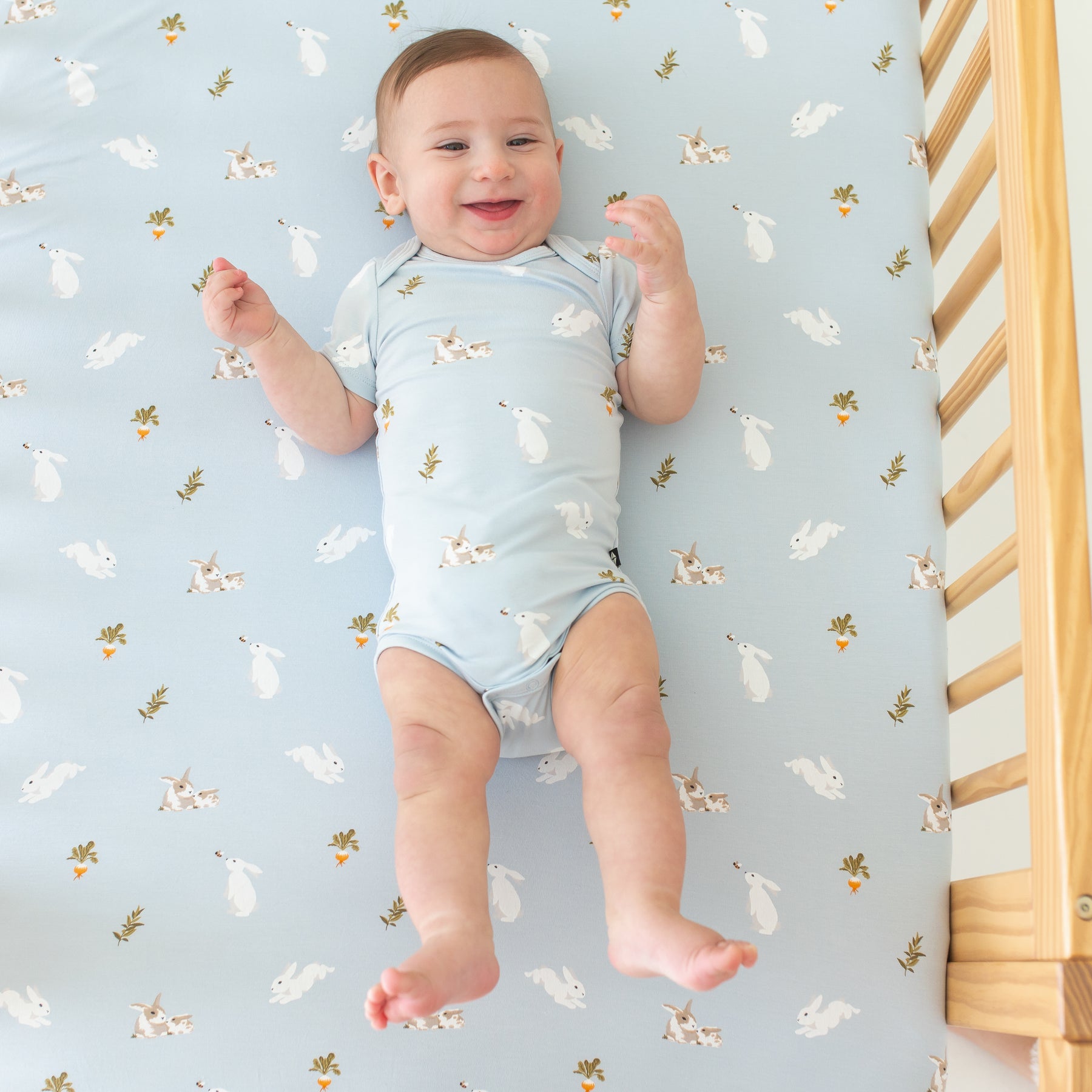 Baby in Bodysuit in Ice Rabbit laying on crib with Ice Rabbit crib sheet