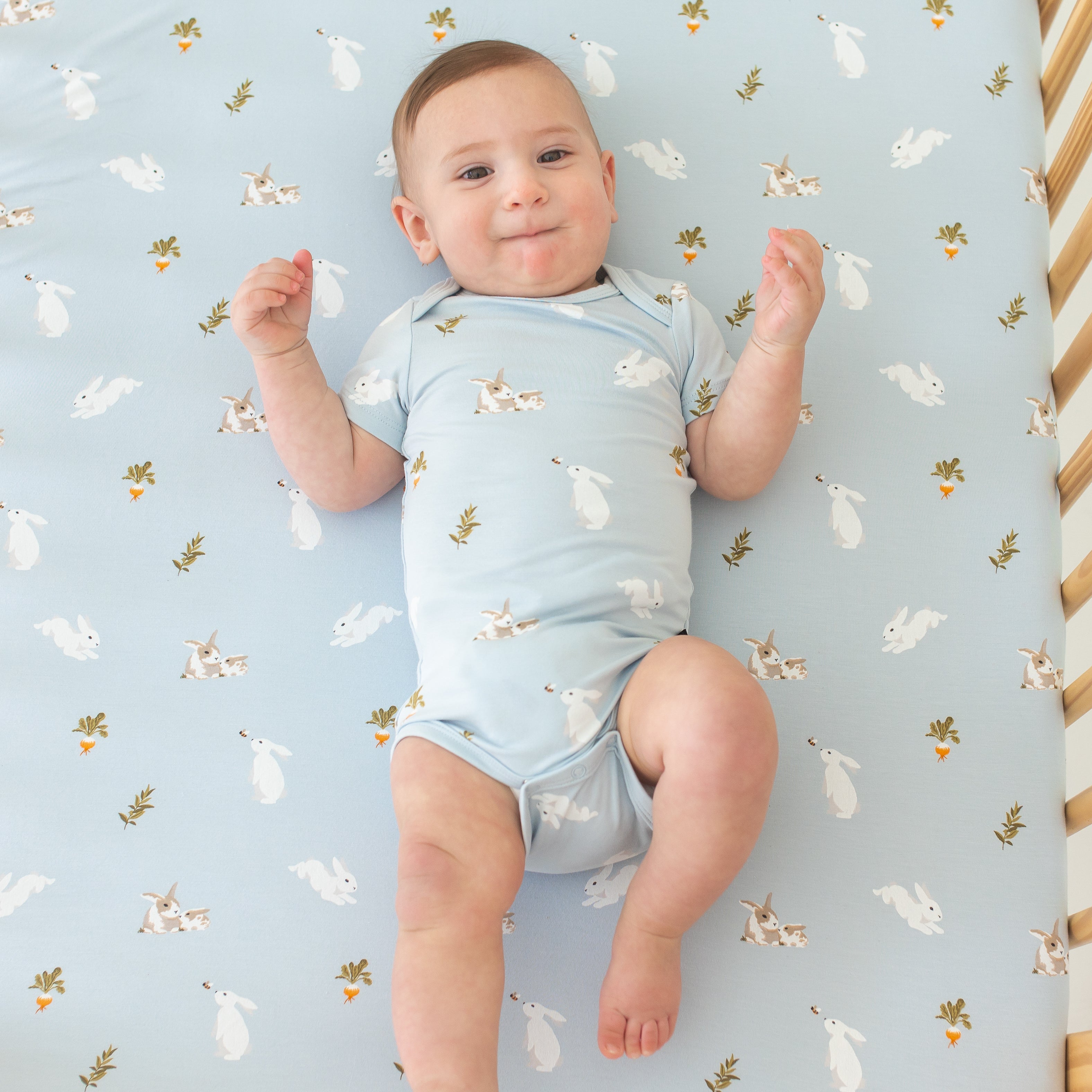 Baby in Bodysuit in Ice Rabbit laying on crib with Ice Rabbit crib sheet