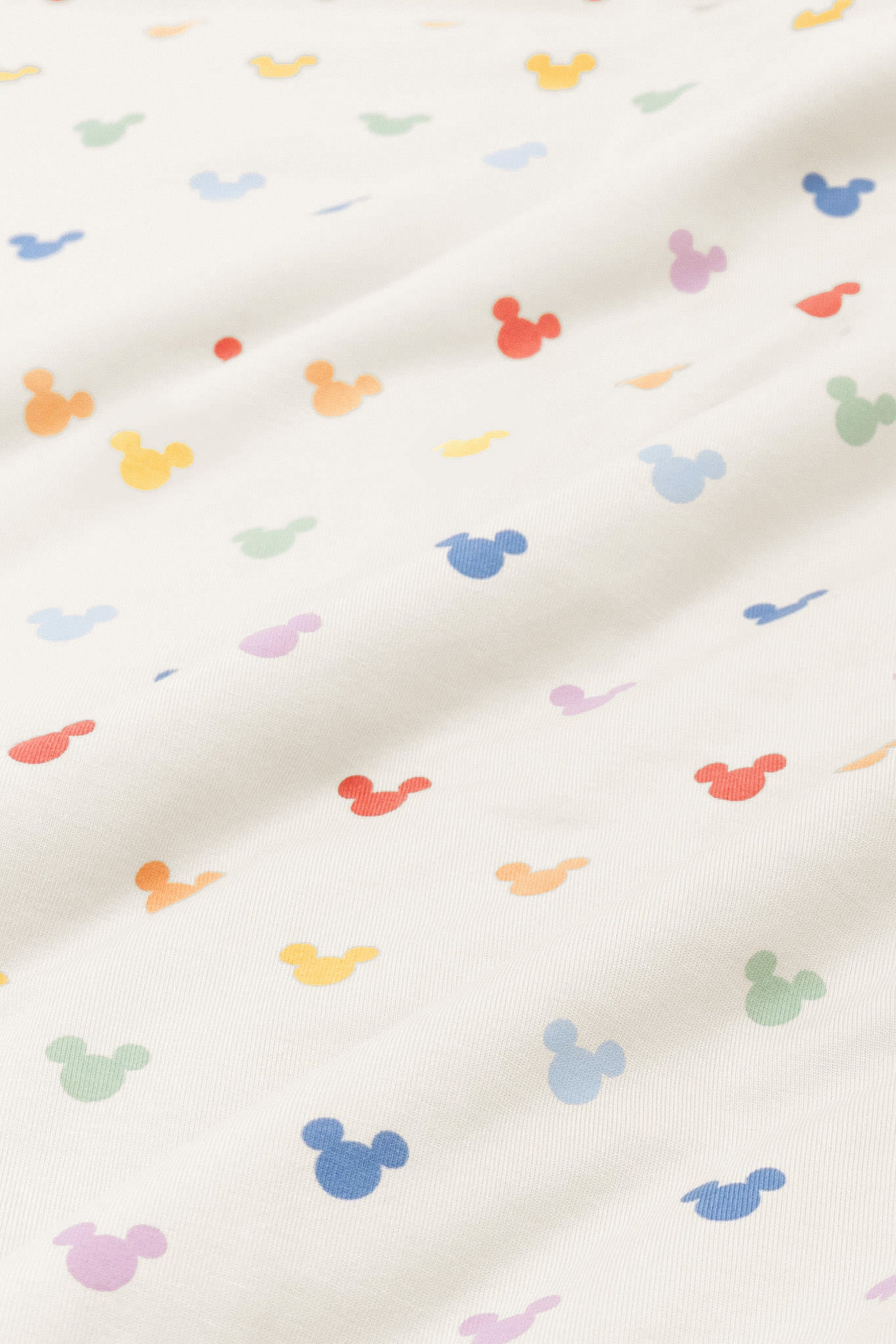Close up of bamboo fabric swatch: An all-over print of classic Mickey Mouse heads in rows of pastel red, pastel orange, yellow, pastel green, sky blue, a muted blue, and a pinkish lilac, over a warm grey background color called Oat.