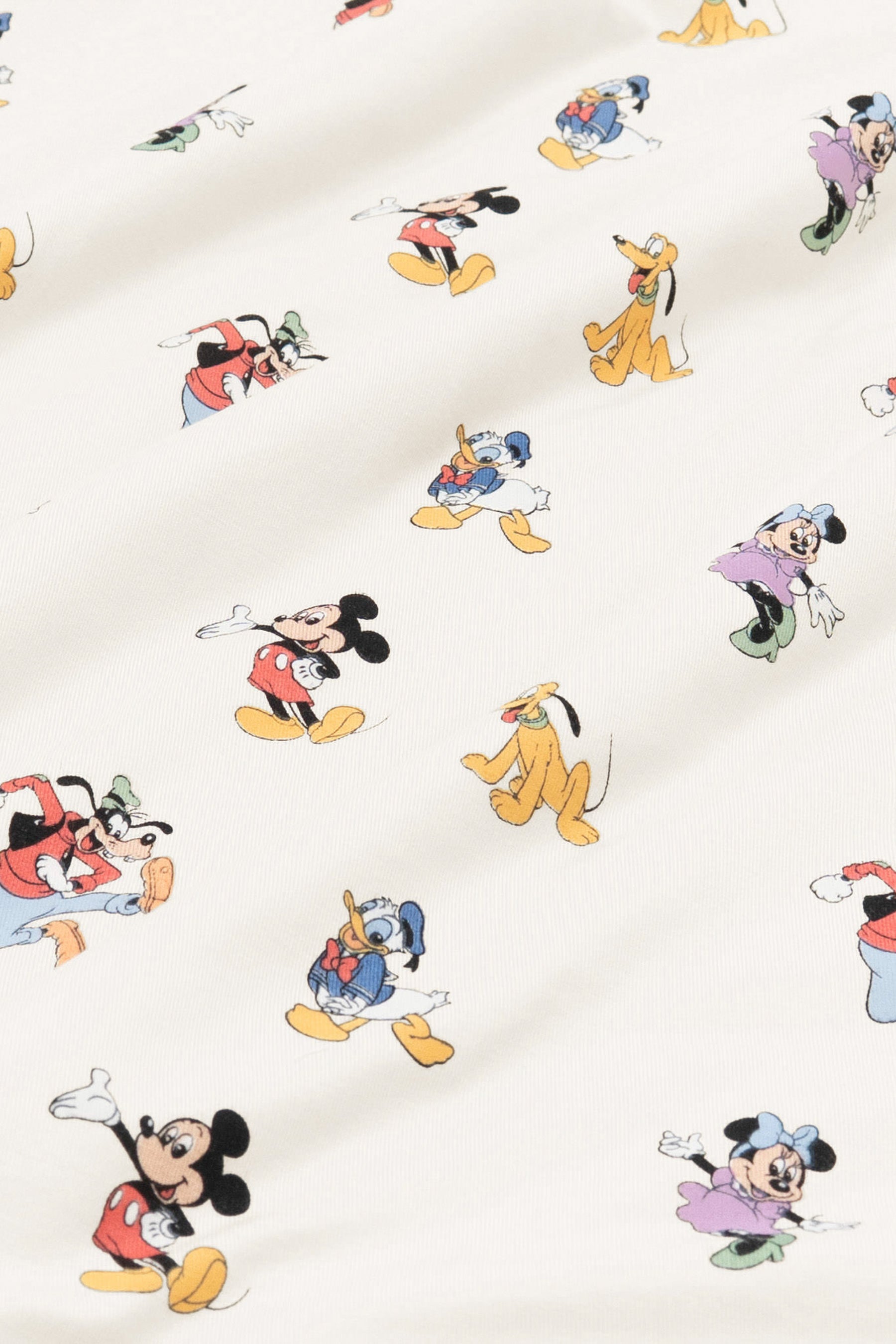Close up of bamboo fabric swatch: An all-over print featuring: Mickey Mouse in his classic red shorts with white buttons and yellow shoes; Minnie Mouse wearing a blue headbow, a pink dress, and green heels; Goofy jumping in the air and wearing a green hat, a red shirt, blue pants, and orange shoes; Pluto wearing a green collar; and Donald Duck in his classic blue sailor outfit and hat, over a warm grey background color called Oat.