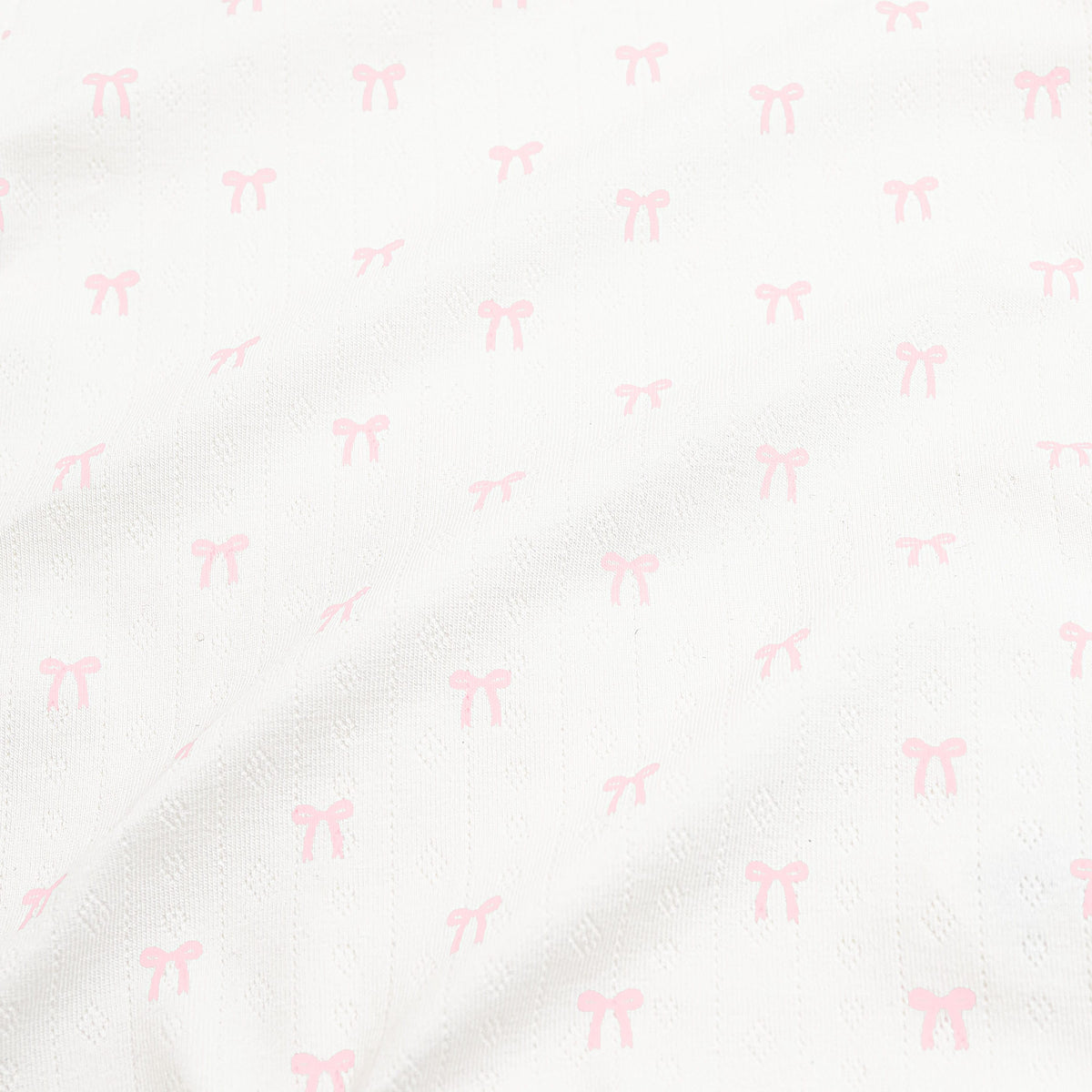 Close up of the pointelle fabric: An all-over print of dainty light pink bows over a white background.