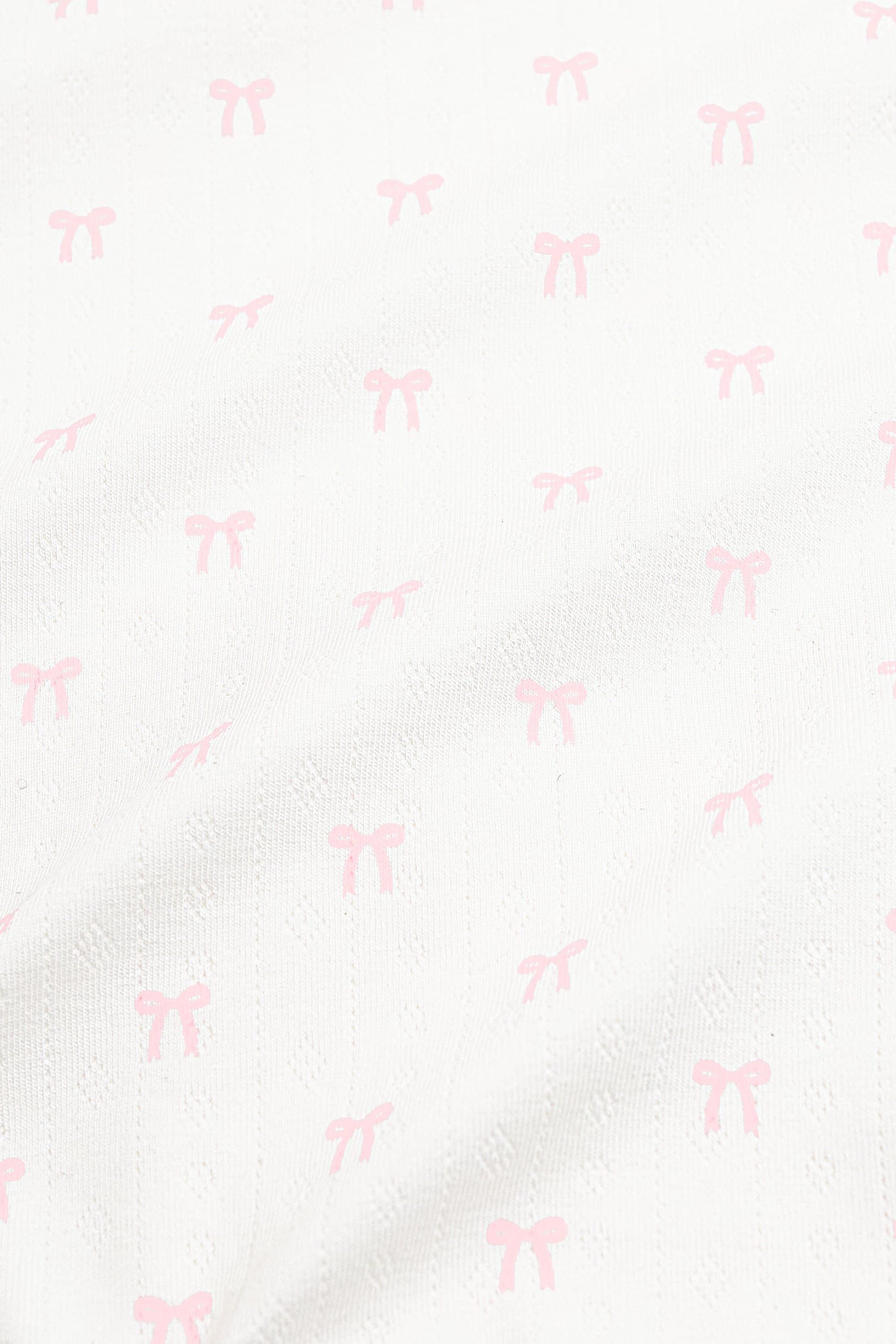 Close up of the pointelle fabric: An all-over print of dainty light pink bows over a white background.