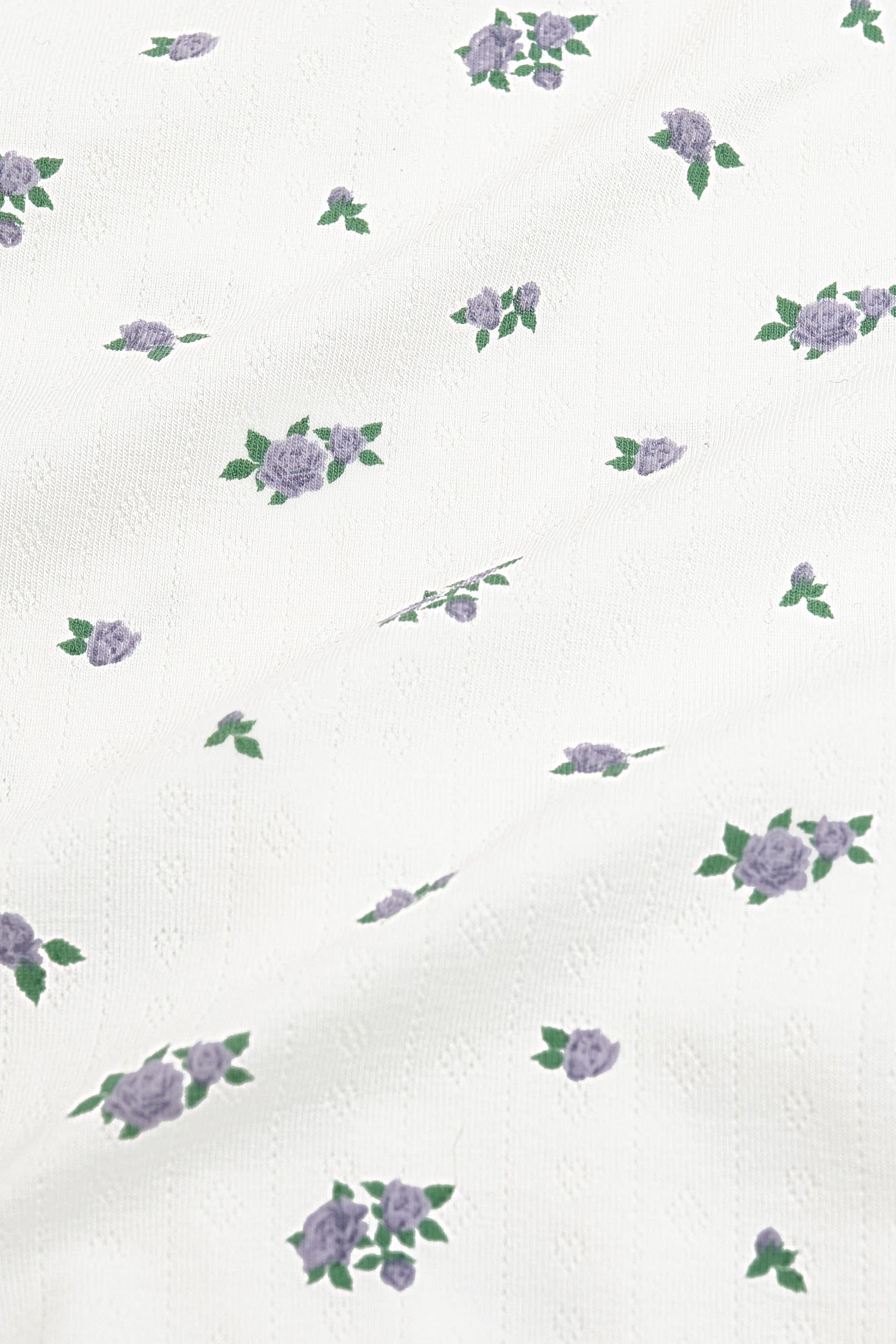 Close up of the pointelle fabric: An all-over print featuring clusters of three purple spray roses with green leaves over a white background.