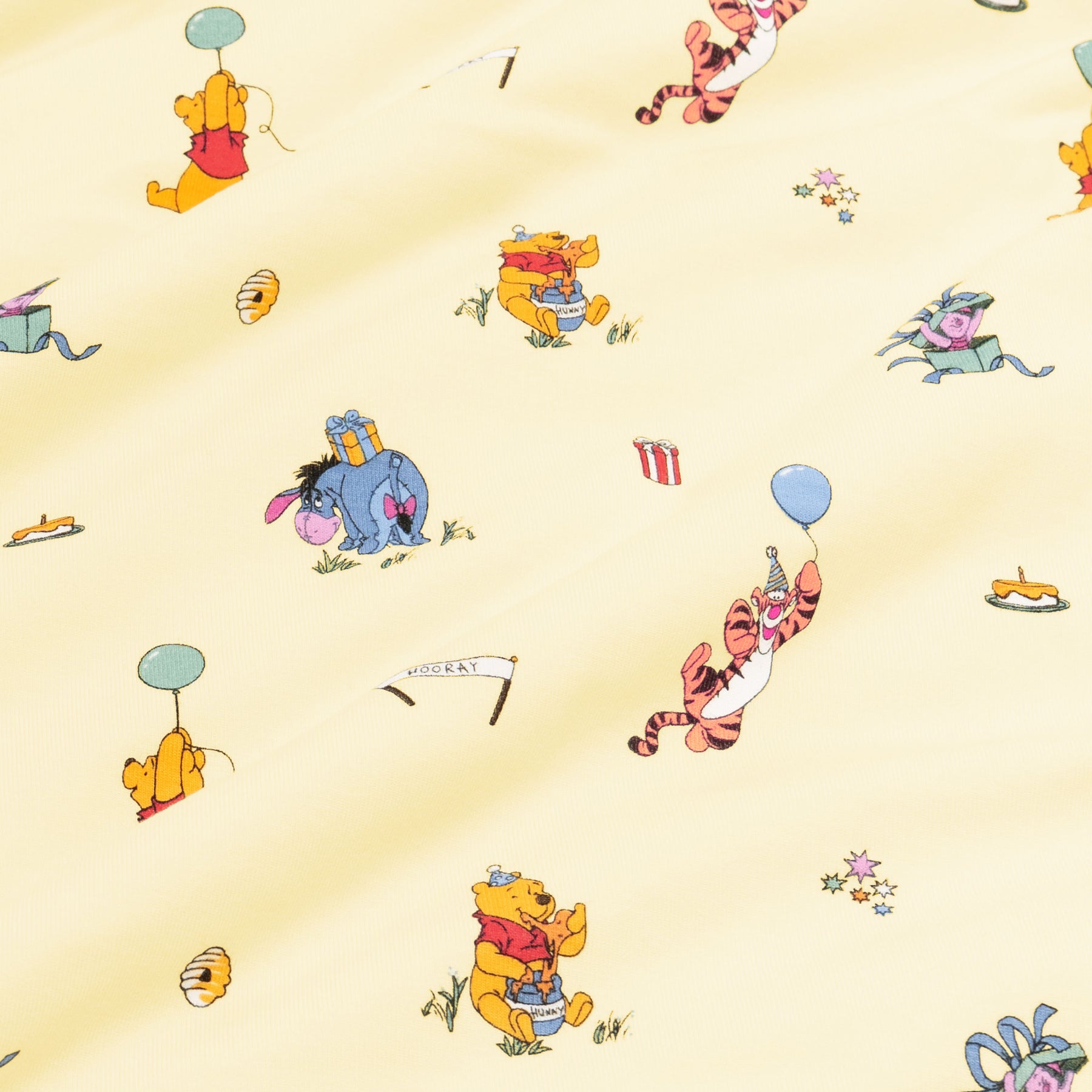 Close up of fabric swatch of the Winnie the Pooh Celebration print  showing the story book characters on a yellow background