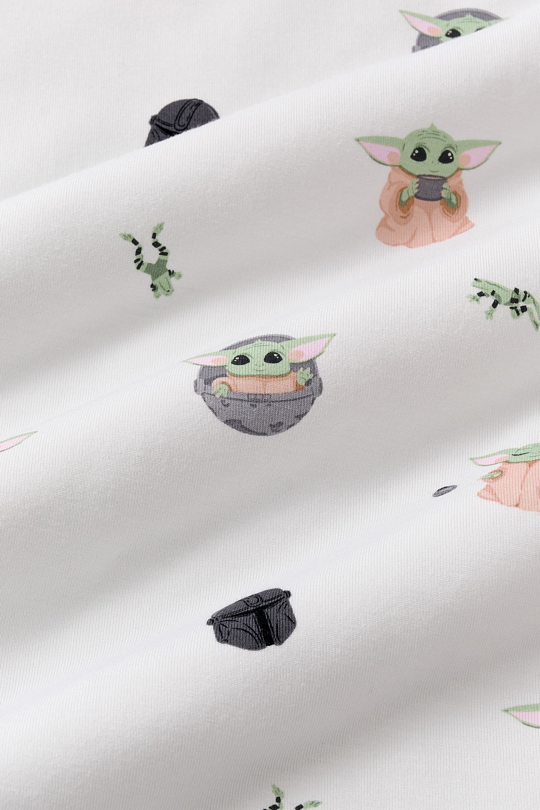 Close up of the bamboo fabric: A repeating, all-over print featuring Grogu in a hover pram; a dark grey Mandalorian helmet; Grogu holding a grey cup; Grogu with his eyes closed, telekinetically manipulating a small silver ball; and leaping green Arges Frogs with black stripes, over a white background.