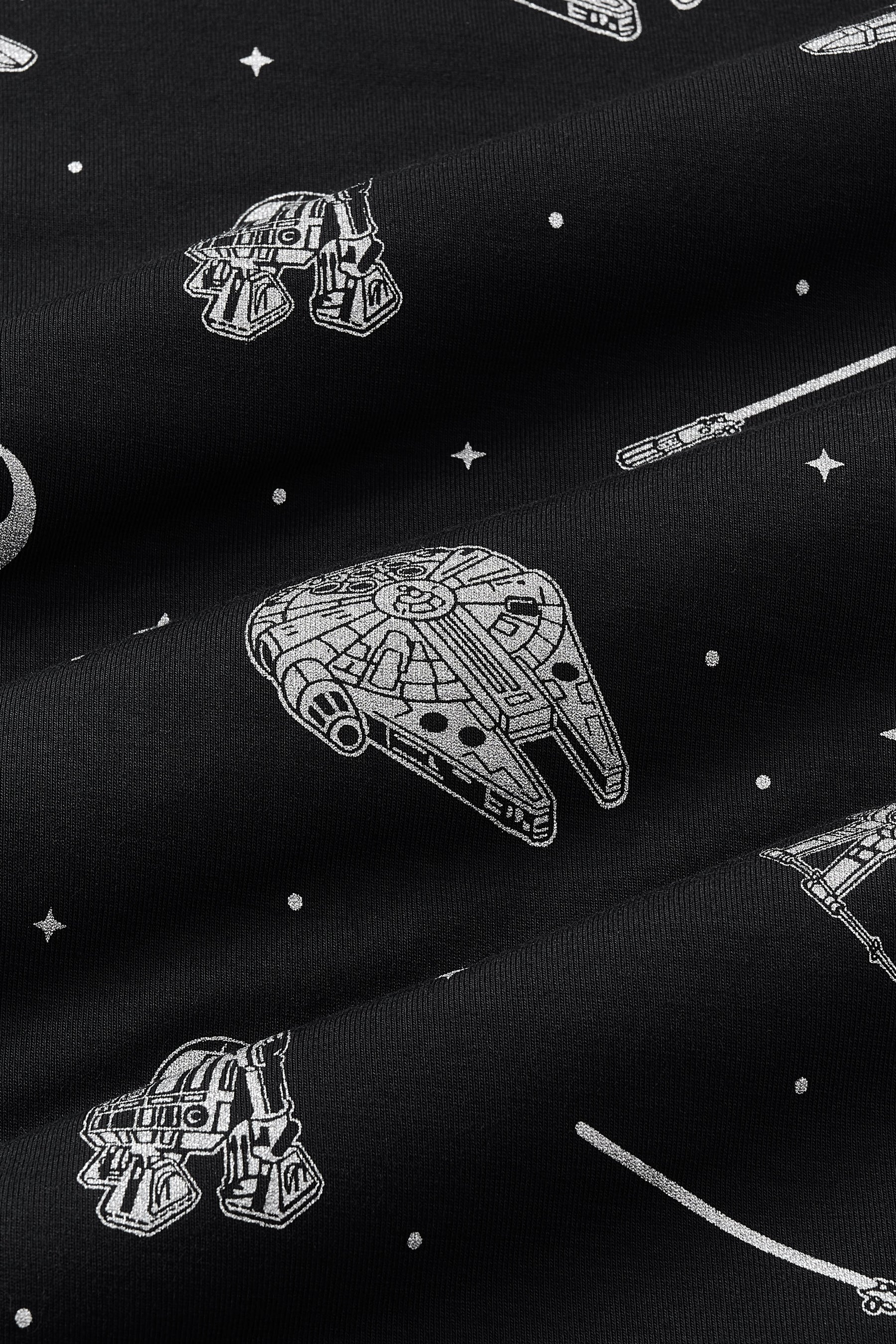 Close up of bamboo fabric: A repeating, monochromatic print featuring: a grey Milennium Falcon; a grey X-wing starfighter; a grey R2-D2; a grey lightsaber; a grey Rebel Alliance starbird symbol; and various grey twinkles and dots, over a black background.