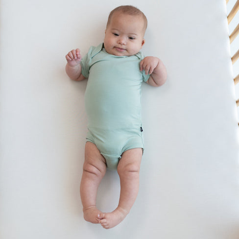 Baby wearing Bodysuit in Sage in a crib