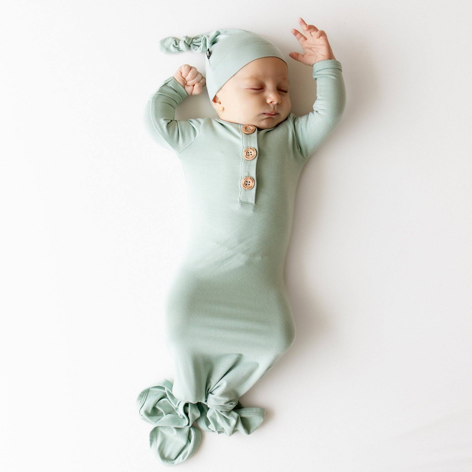 Baby asleep wearing kyte baby knotted gown and hat set in a sage green