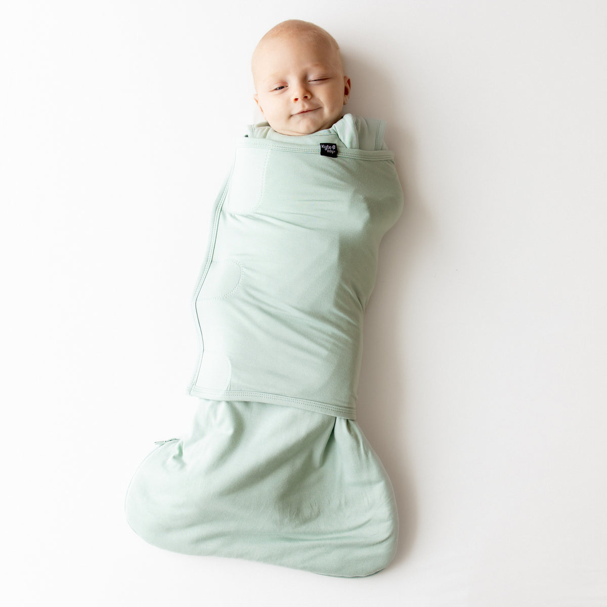 Baby swaddled in a light green swaddler on a white background