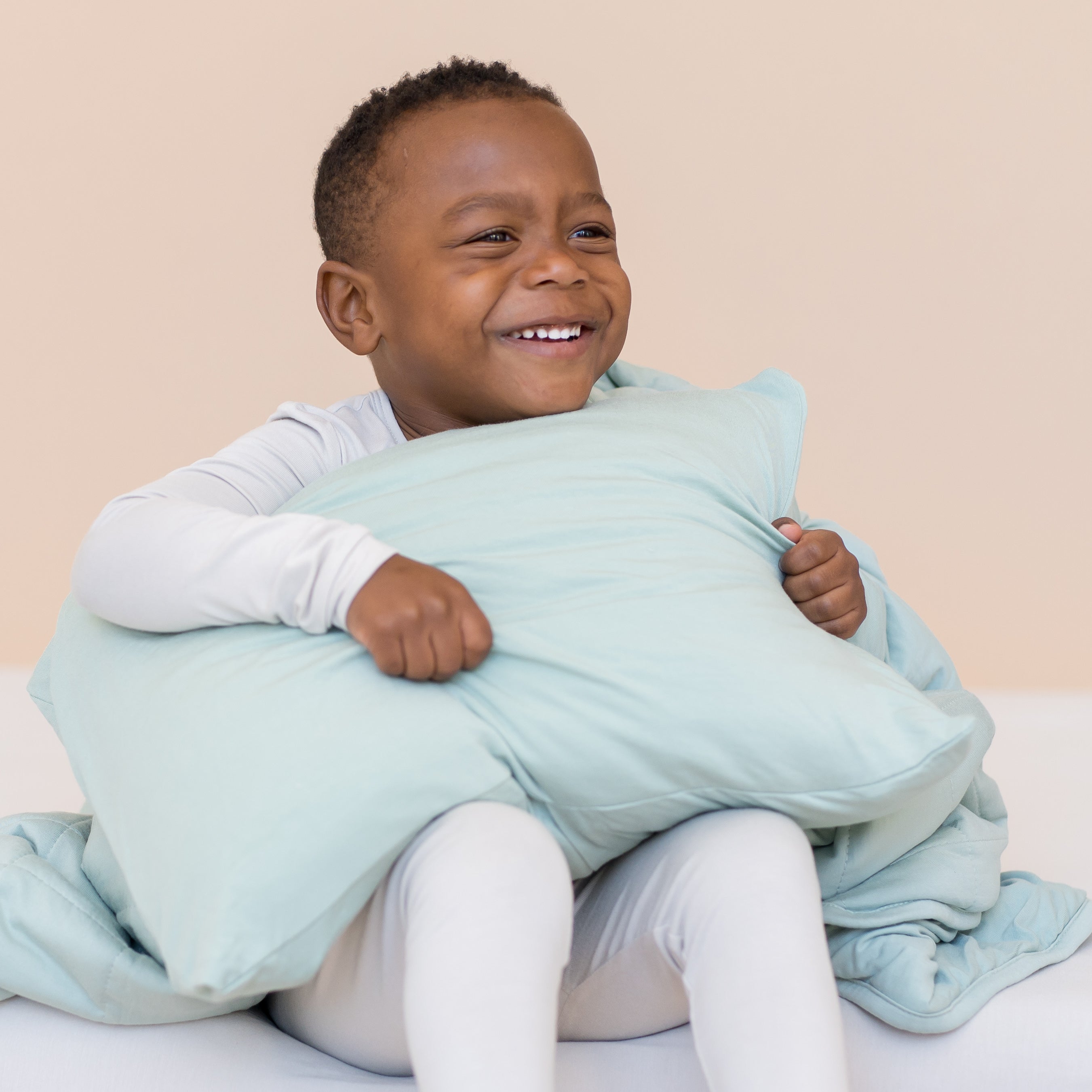 Young boy holding a sage green toddler pillow