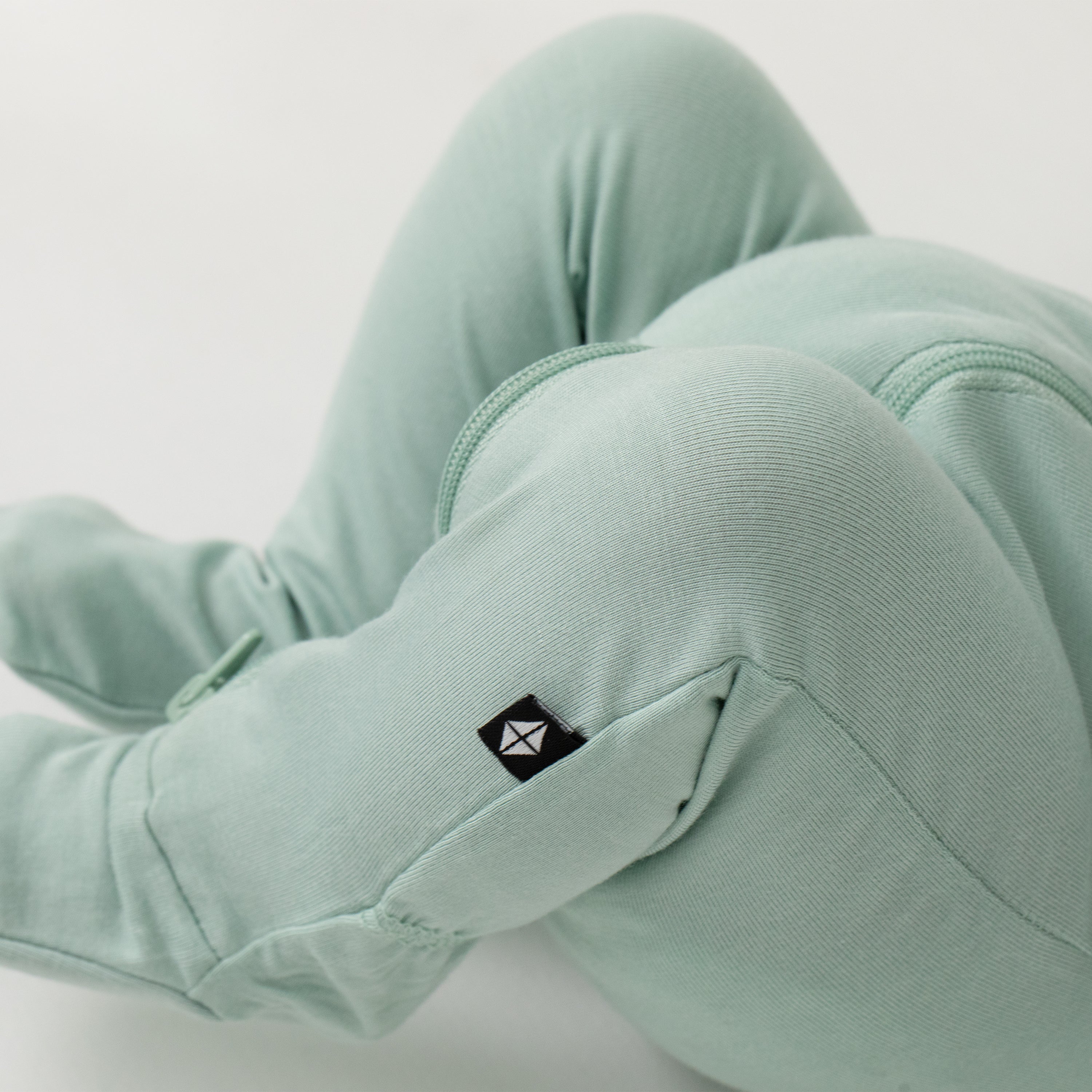 Close up of the black Kyte Baby logo tag on the Zippered Footie in Sage