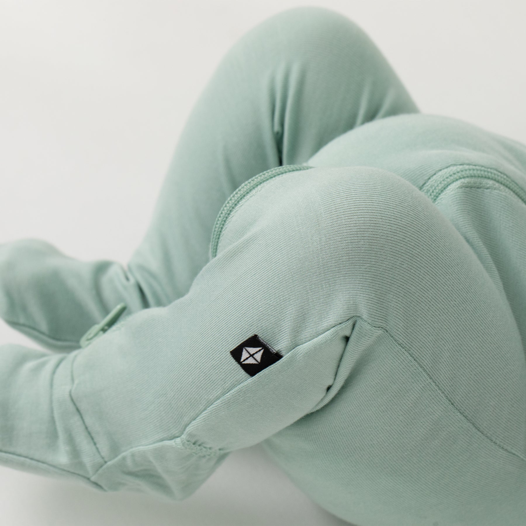 Close up of the black Kyte Baby logo tag on the Zippered Footie in Sage