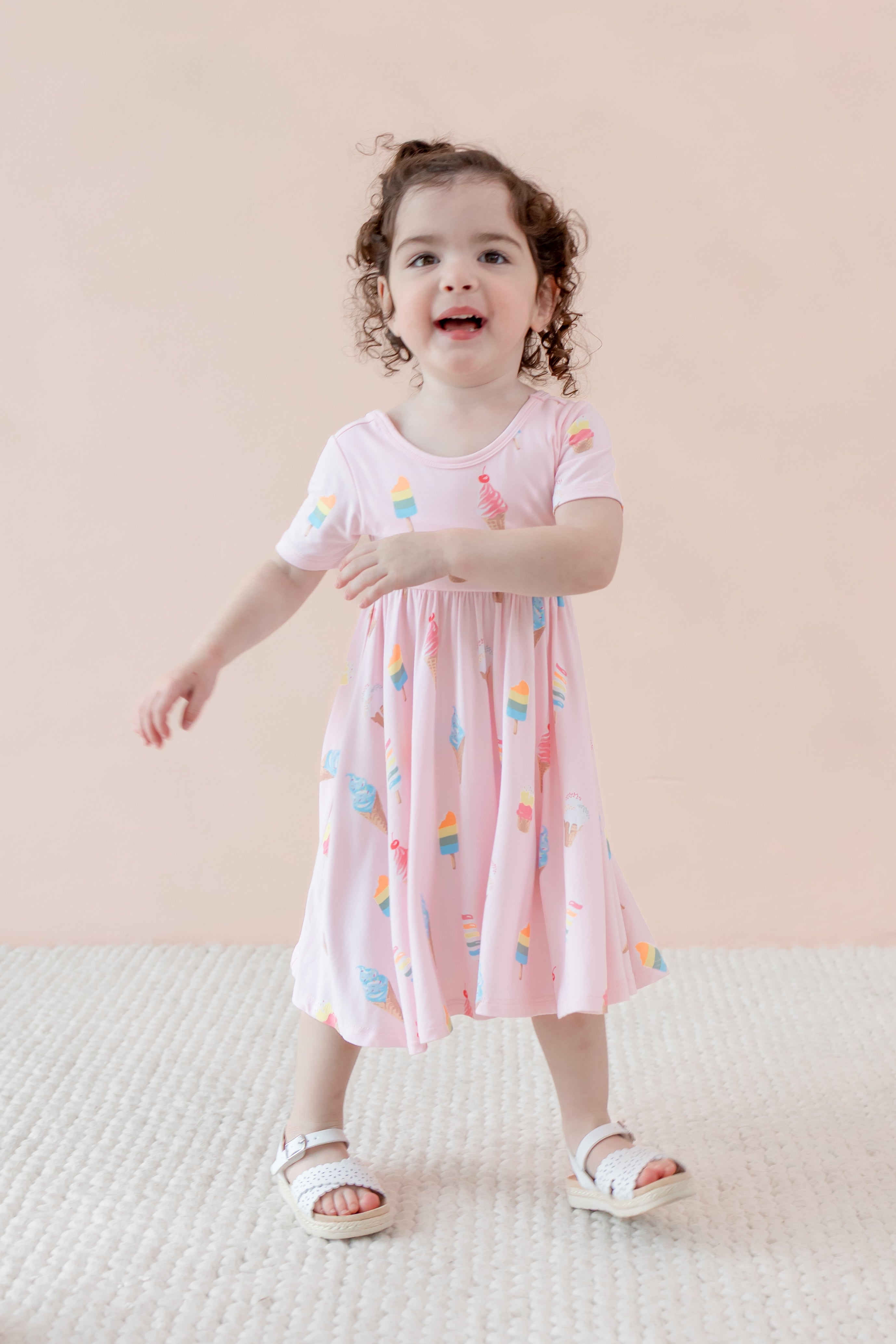 Child posing in Twirl Dress with Sakura Ice Cream print wearing sandles on a beige background