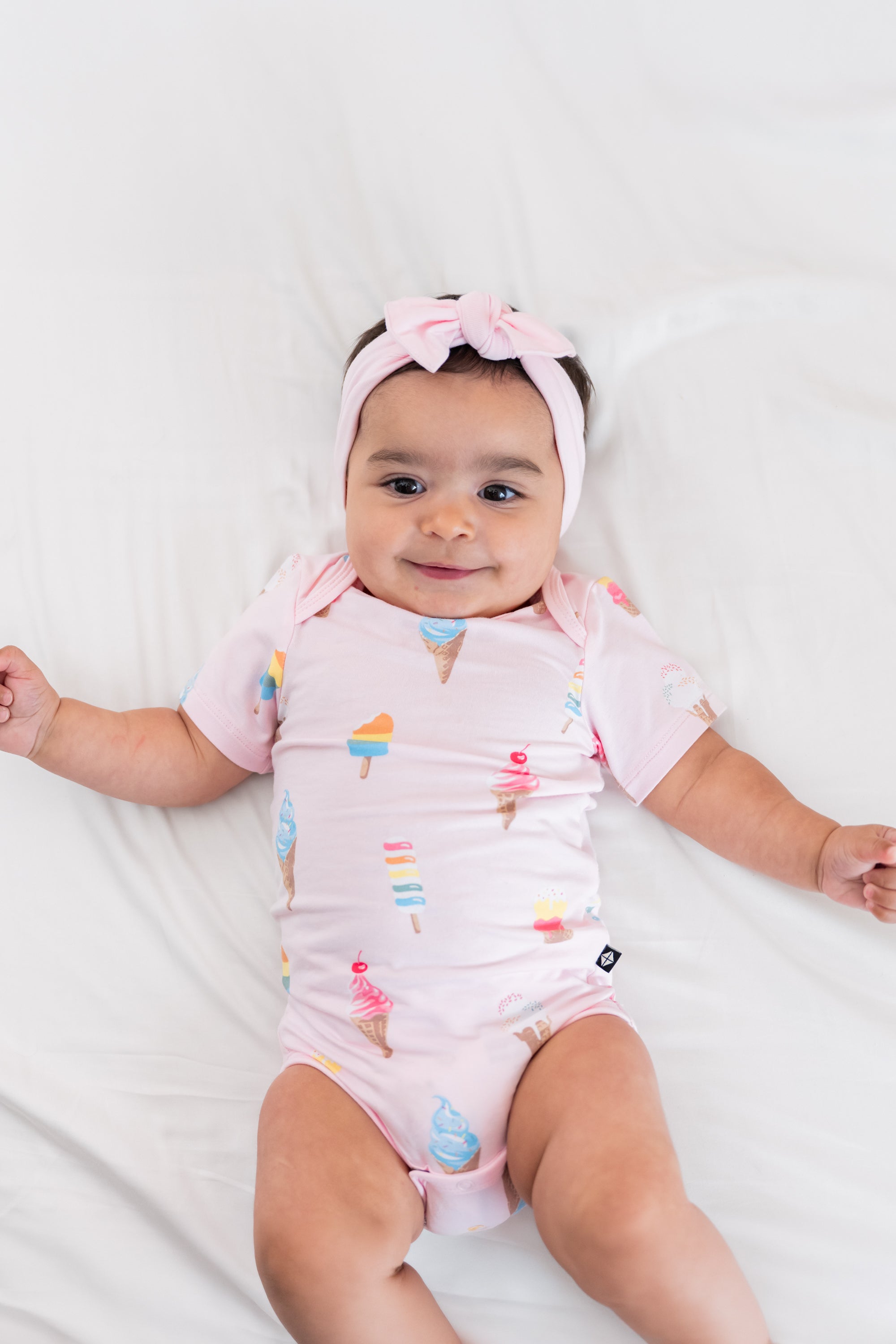 Baby wearing a Sakura Ice cream print Bodysuit with a pink bow headband on a beige background