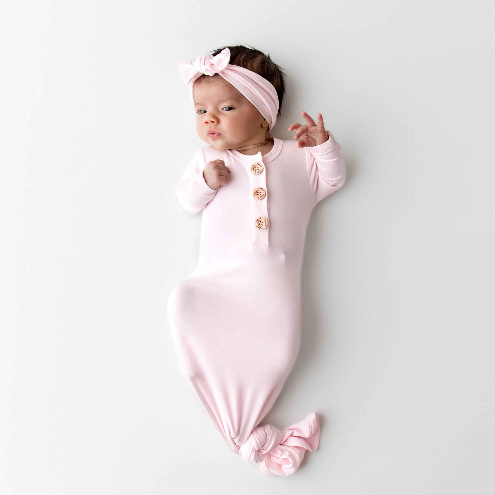 Newborn baby in a light pink knotted gown and matching bow headband 