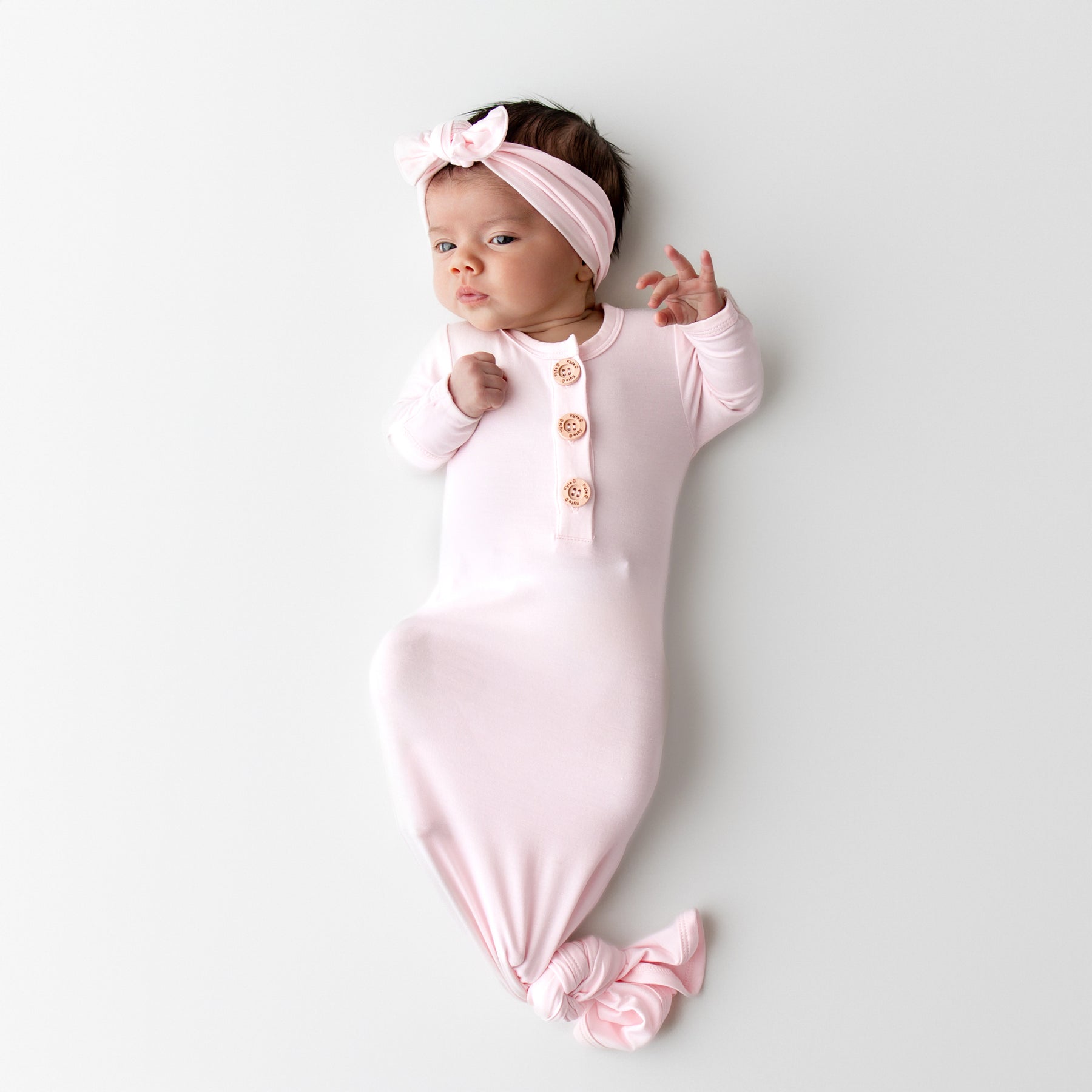 Newborn baby in a light pink knotted gown and matching bow headband 