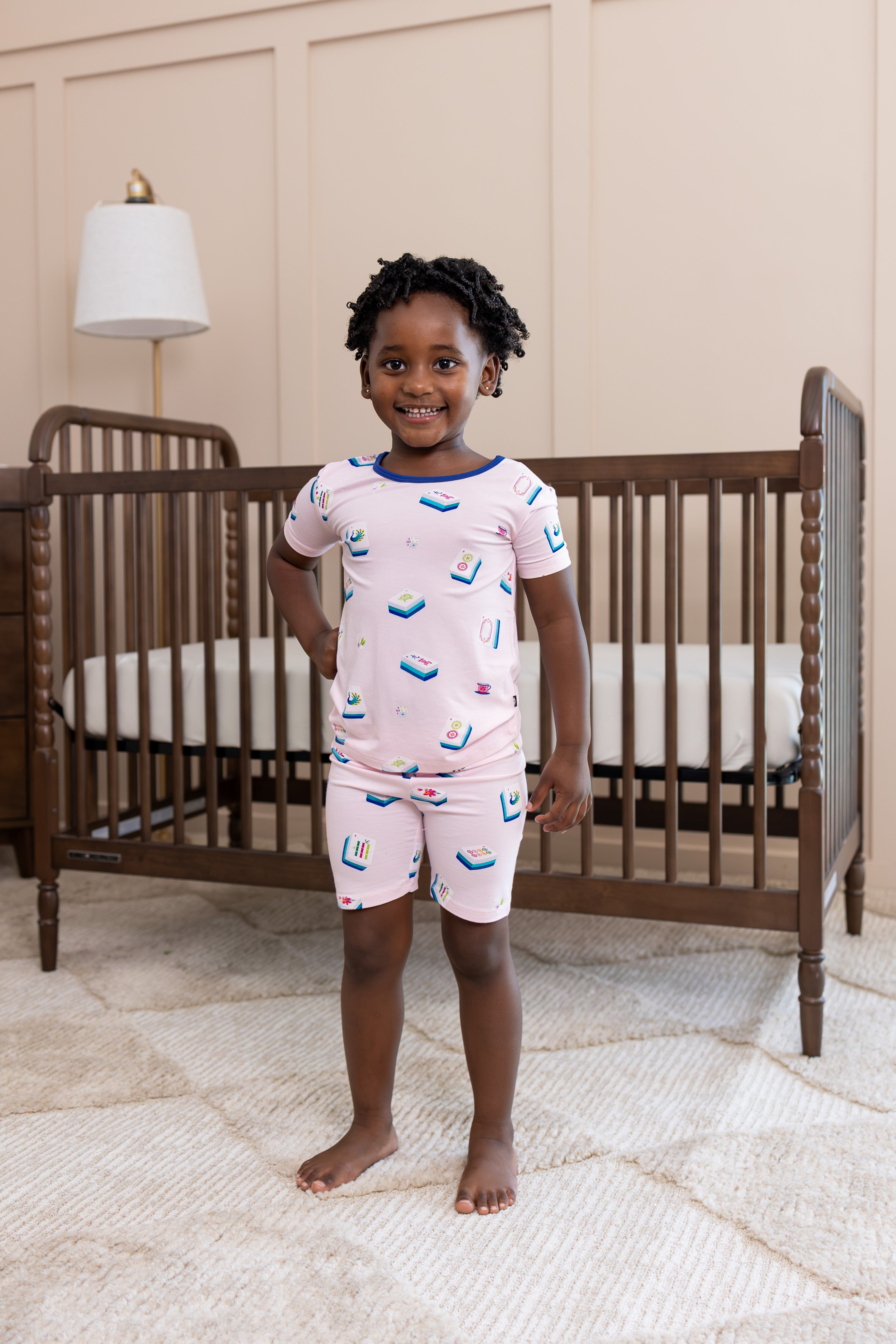 Girl wearing Short Sleeve Pajamas in Sakura Mahjong print standing in front of a crib