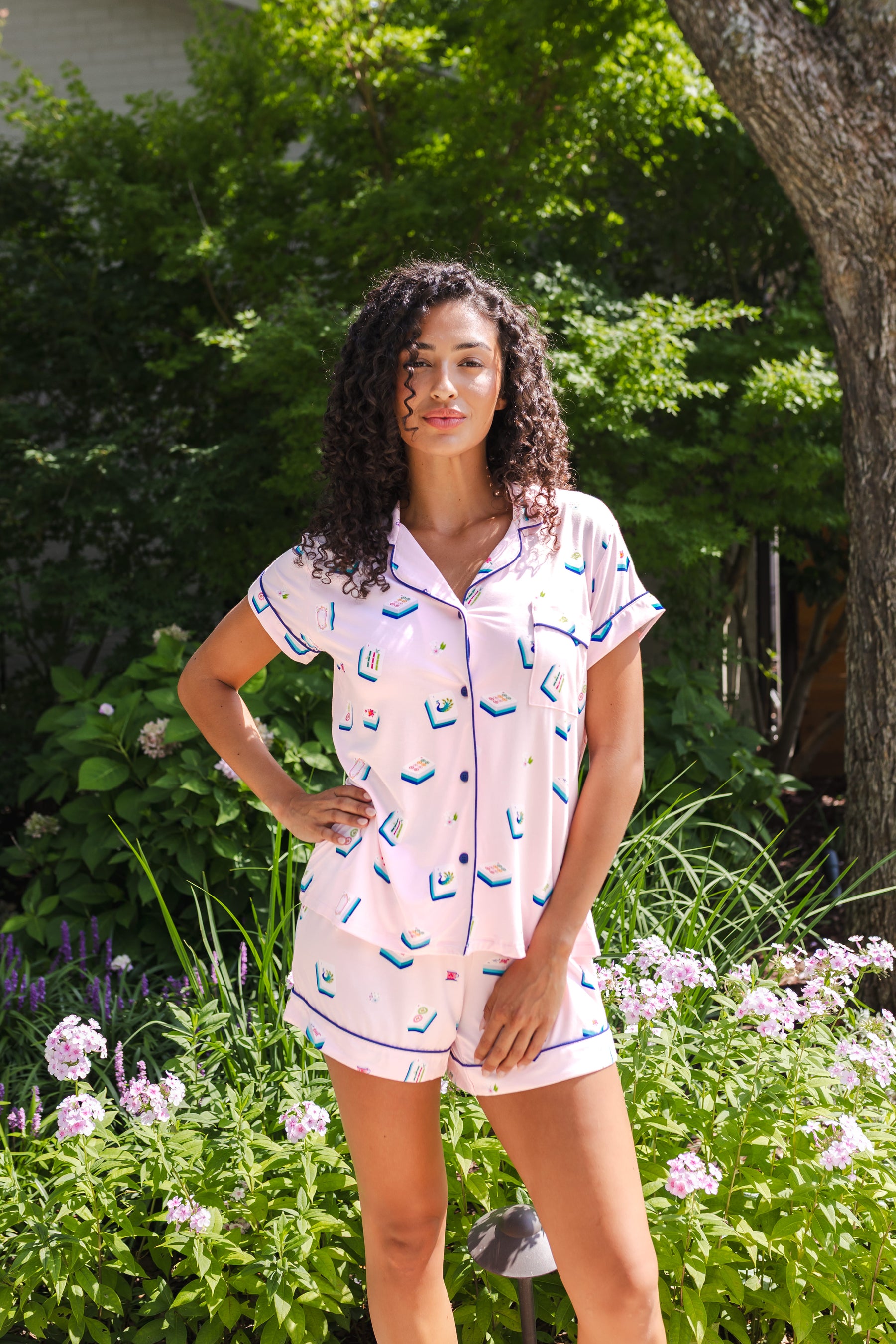 woman wearing pink short sleeve pajama set with mahjong tile print standing outdoors in greenery