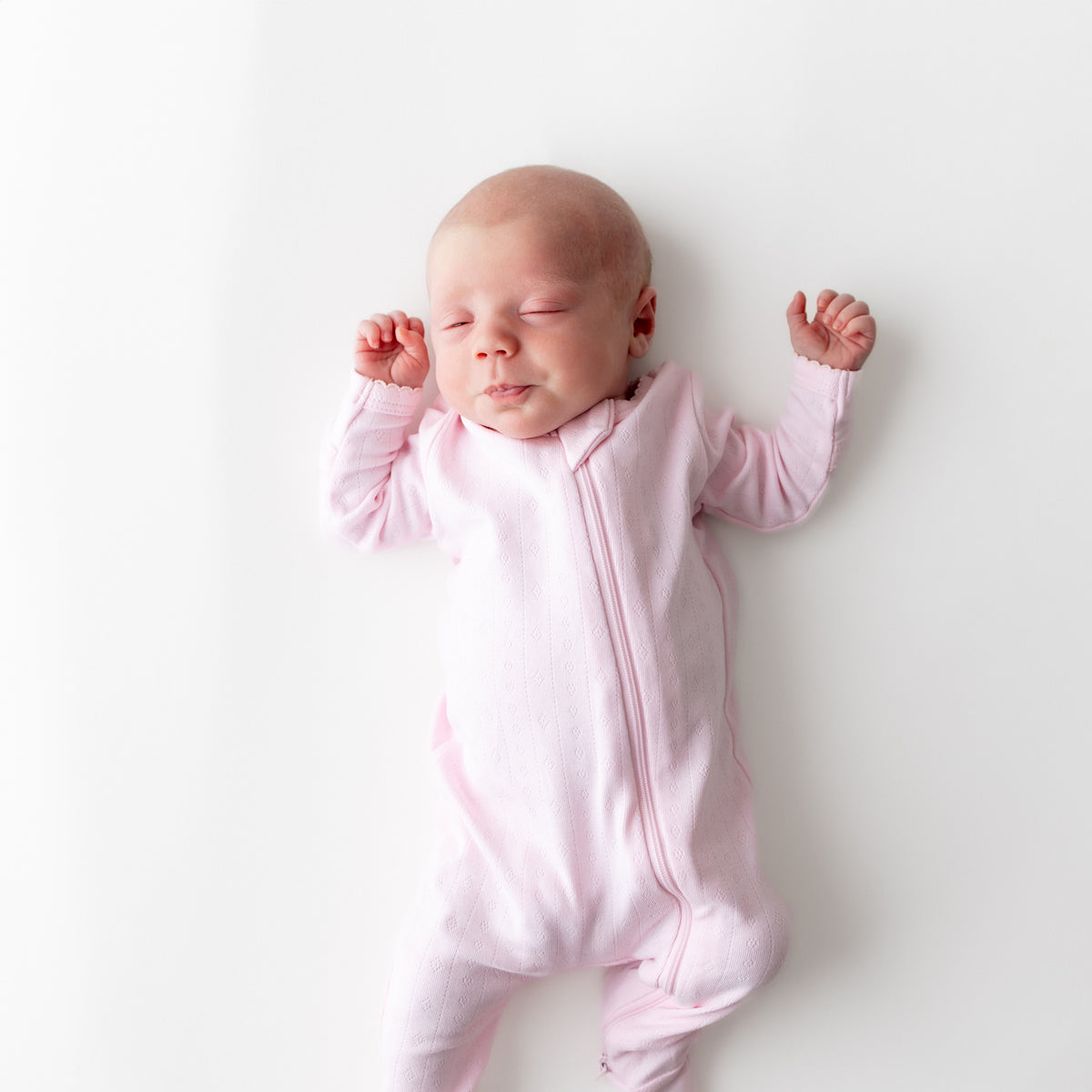 Close up of a newborn wearing the Pointelle Zippered Footie in Sakura