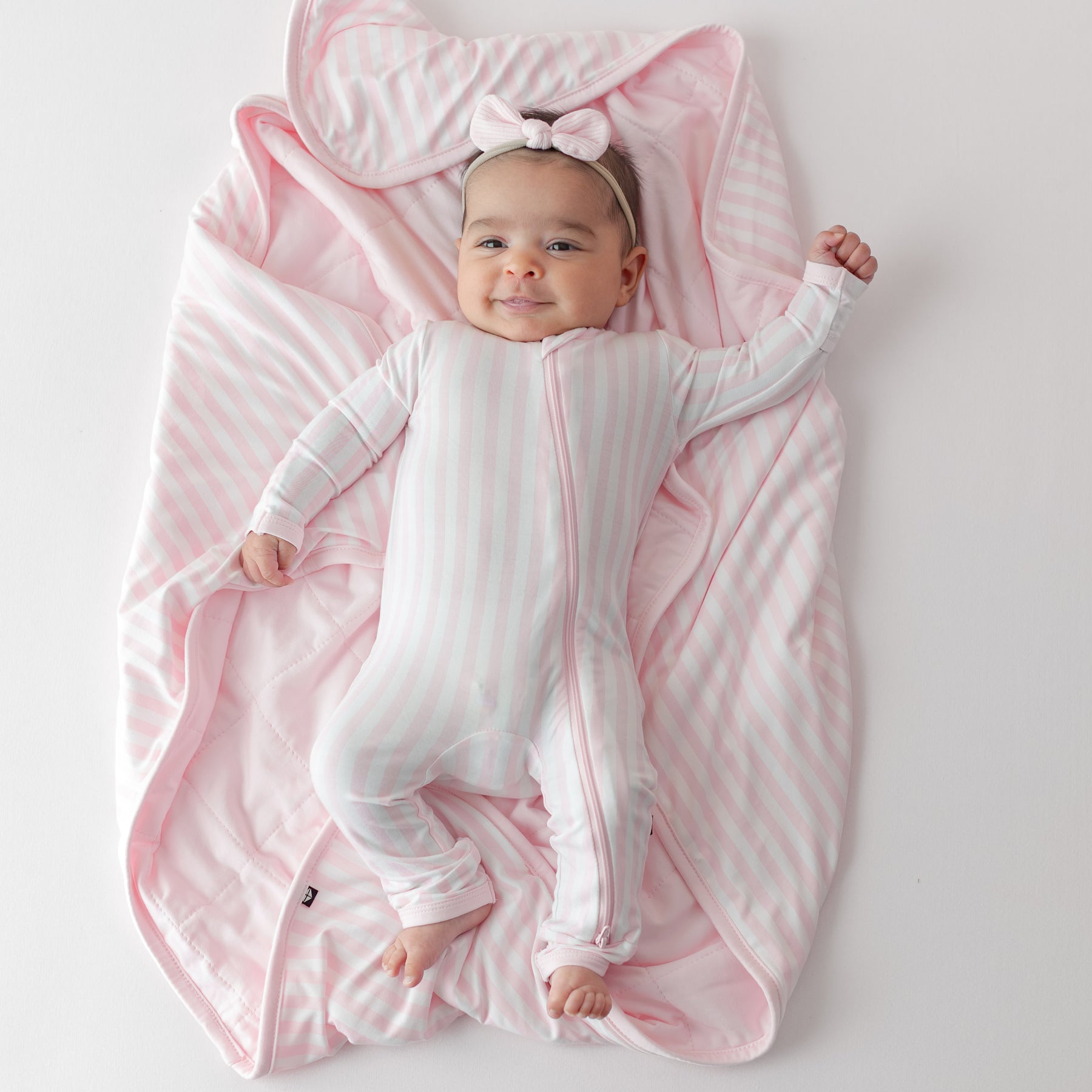 Infant girl laying on the buttery soft Baby Blanket in Small Sakura Stripe 1.0 wearing a matching zippered romper