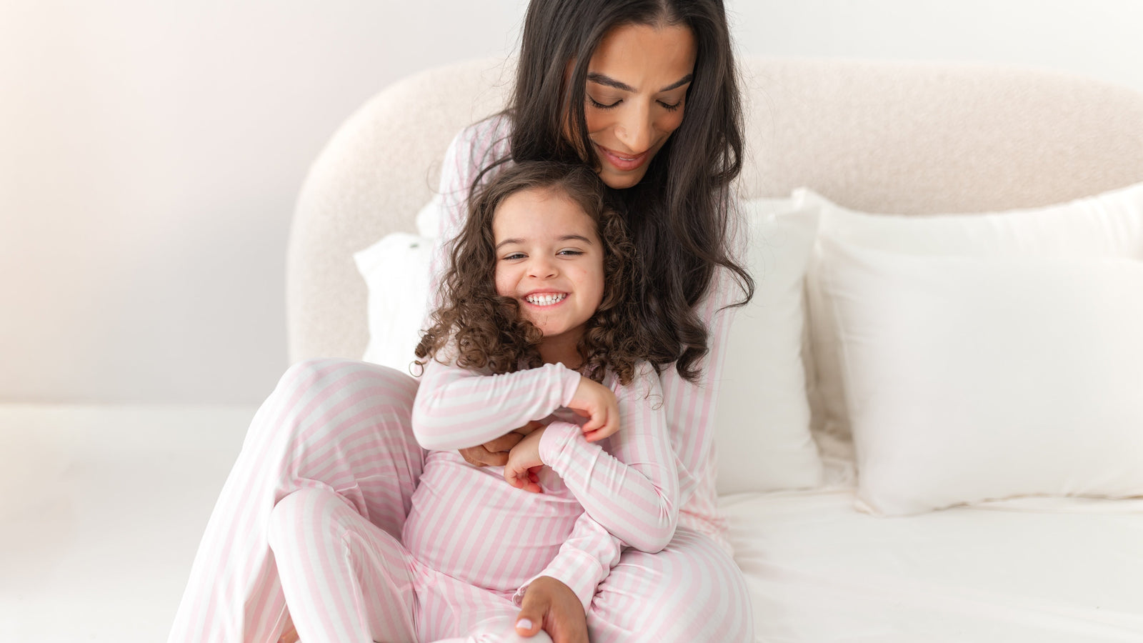 Mom and toddler snuggled in a white bed with matching light pink striped pajamas