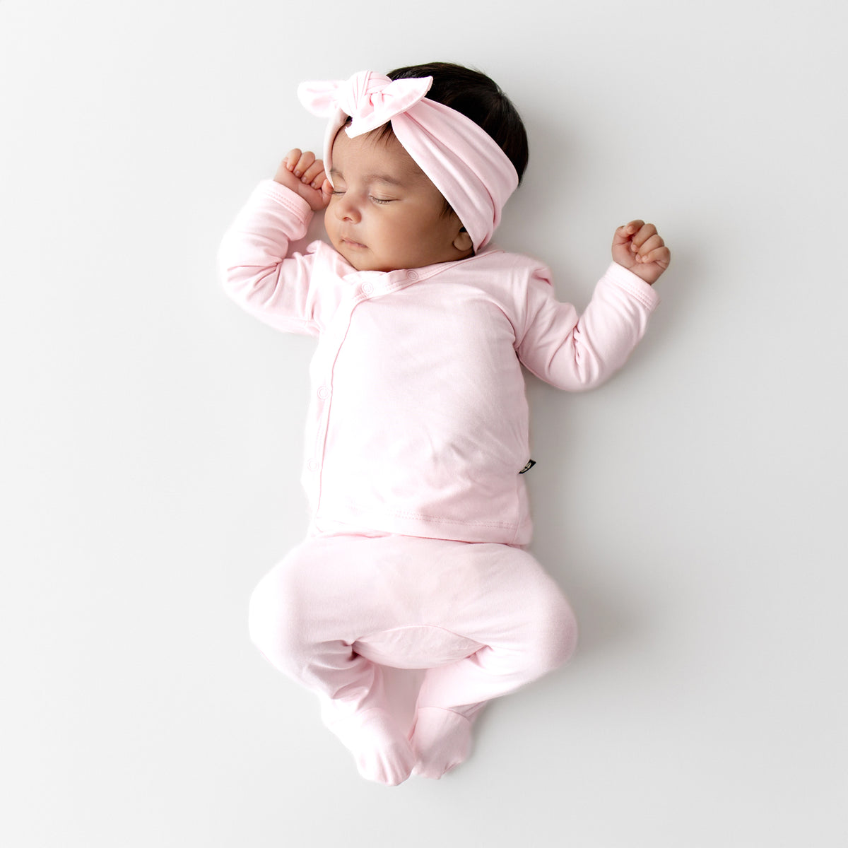 Newborn baby wearing a kyte baby take me home set in a light pink color with matching bow