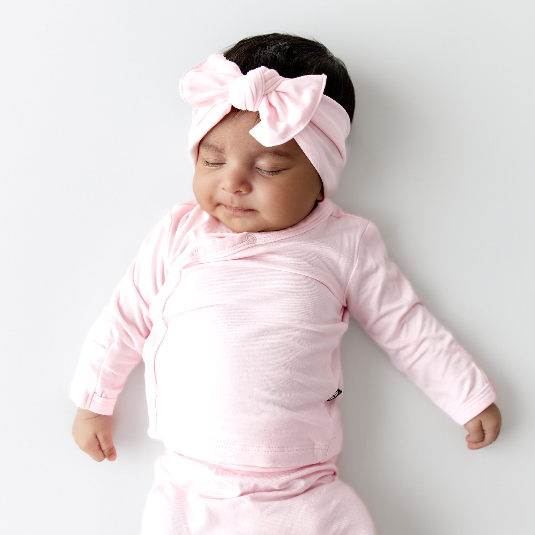 Baby in pink outfit with a large bow headband on a light gray background