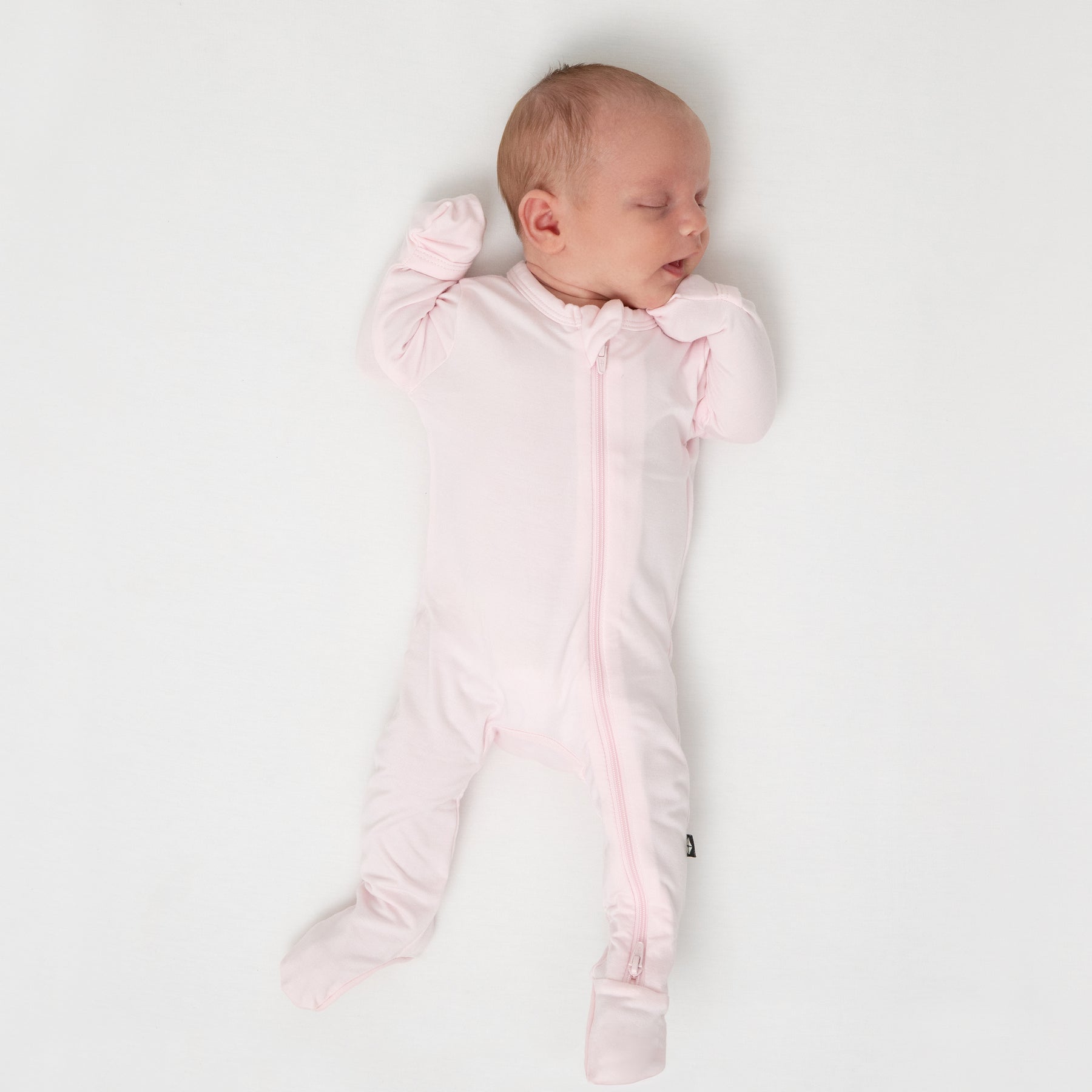 Sleeping infant laying on a white crib sheet wearing the Zippered Footie in Sakura
