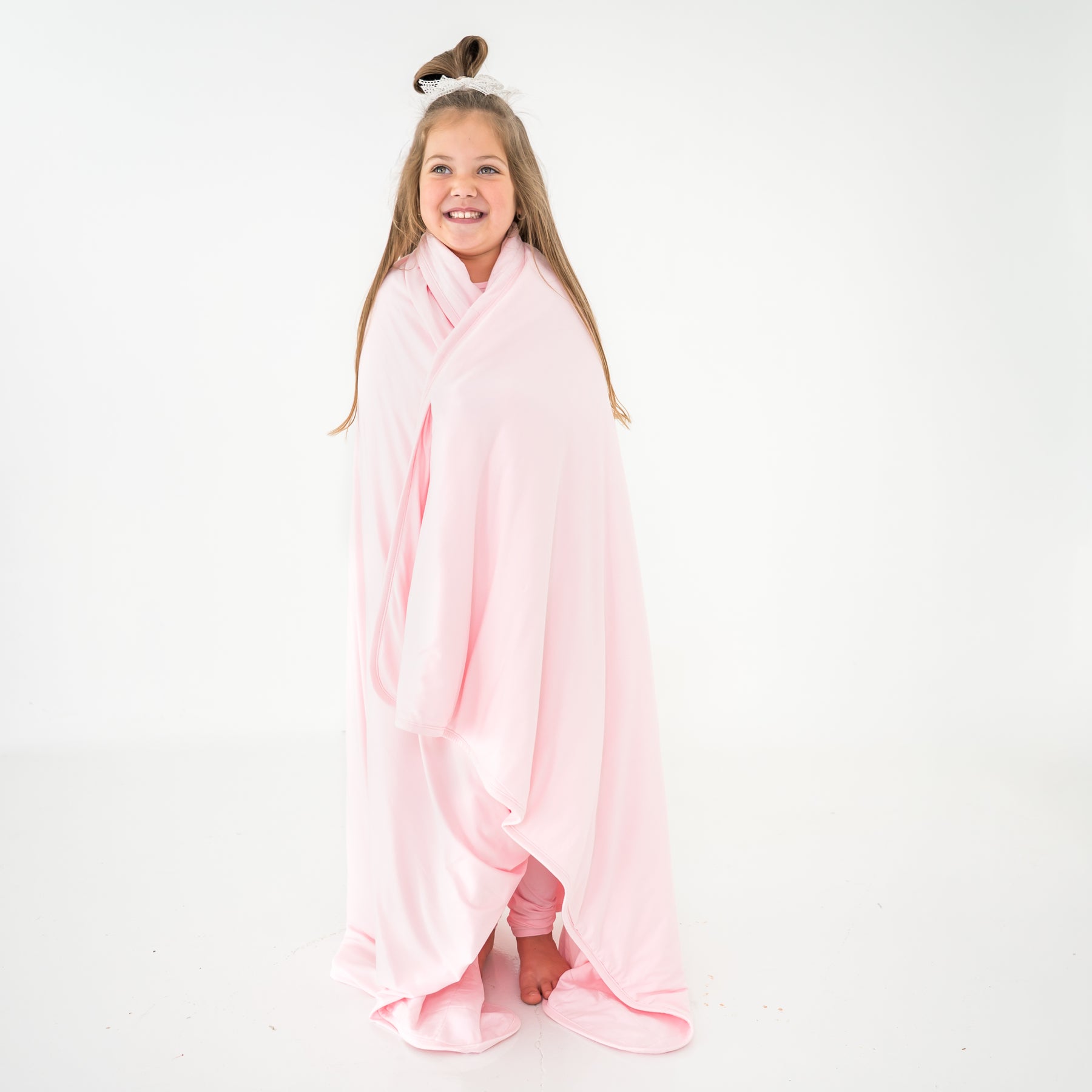 Young girl wrapped in a pink bamboo quilted blanket on a white background