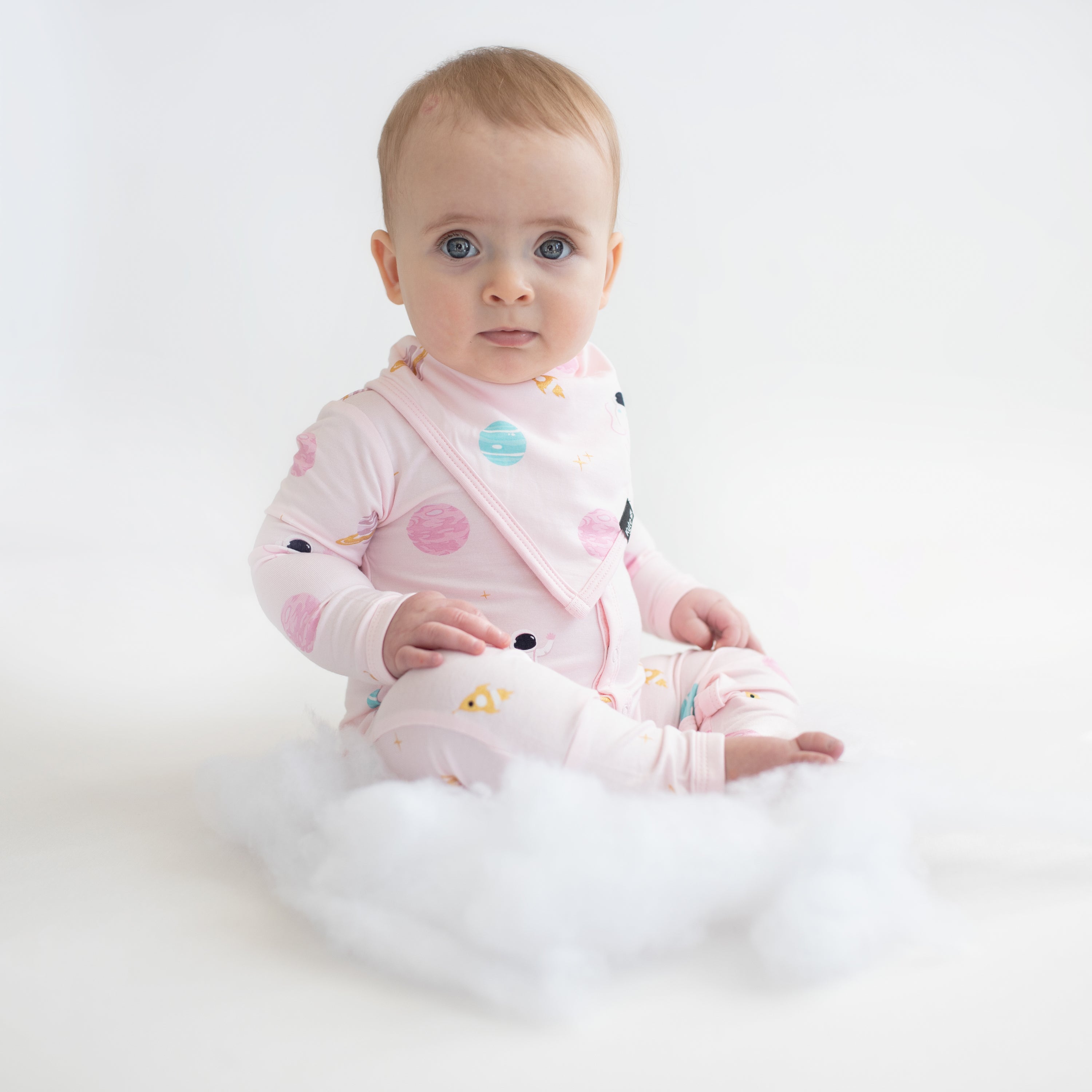 baby wearing sakura space bib and romper sitting on a pretend cloud