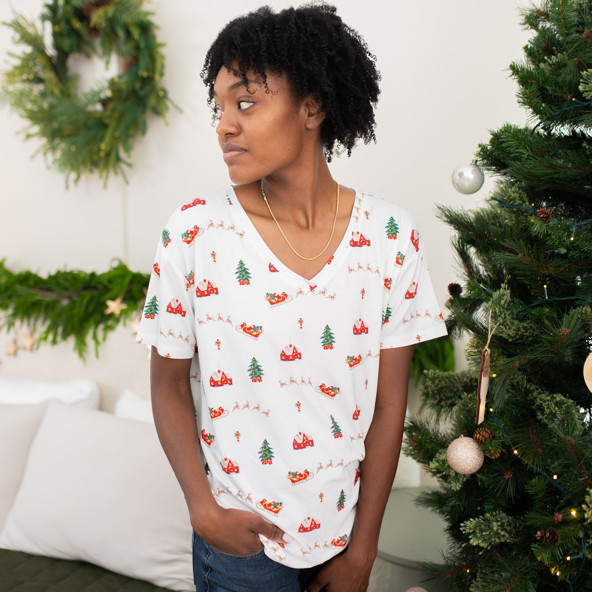 Female model standing looking off to the side wearing the omen's Relaxed Fit V-Neck in Santa Sleigh with one hand in her jeans pocket