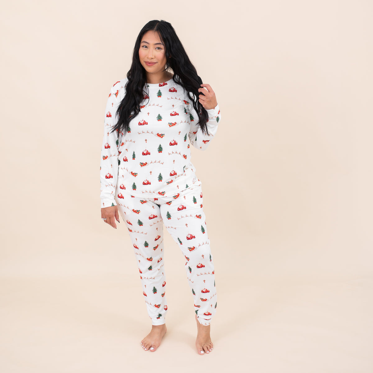 Female model standing in front of a light beige backdrop wearing the Women's Jogger Pajama Set in Santa Sleigh