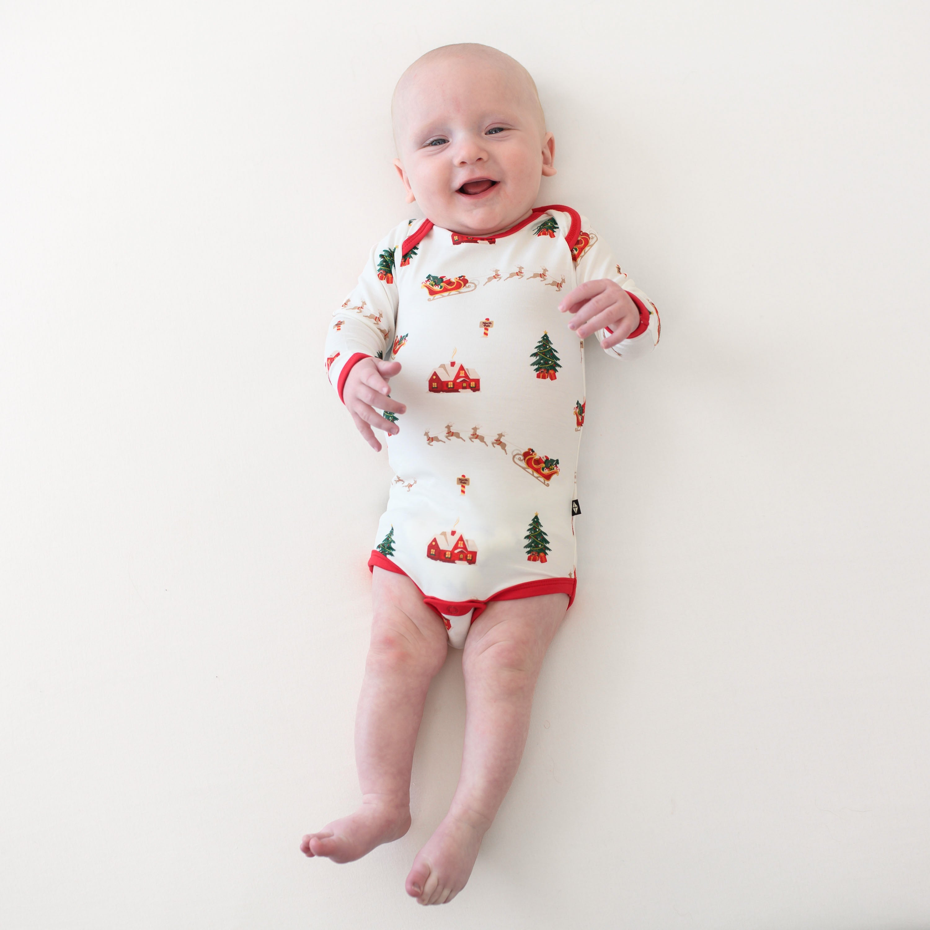 Infant laying on a light neutral backdrop wearing the Long Sleeve Bodysuit in Santa Sleigh