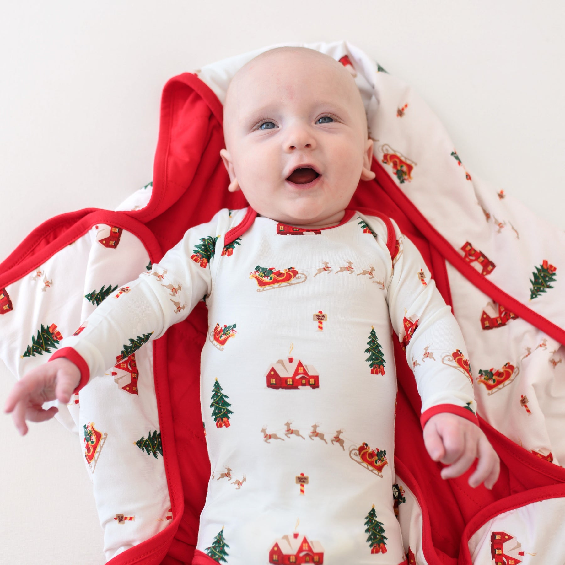 Close up of the Long Sleeve Bodysuit in Santa Sleigh shown on an infant laying on a matching blanket