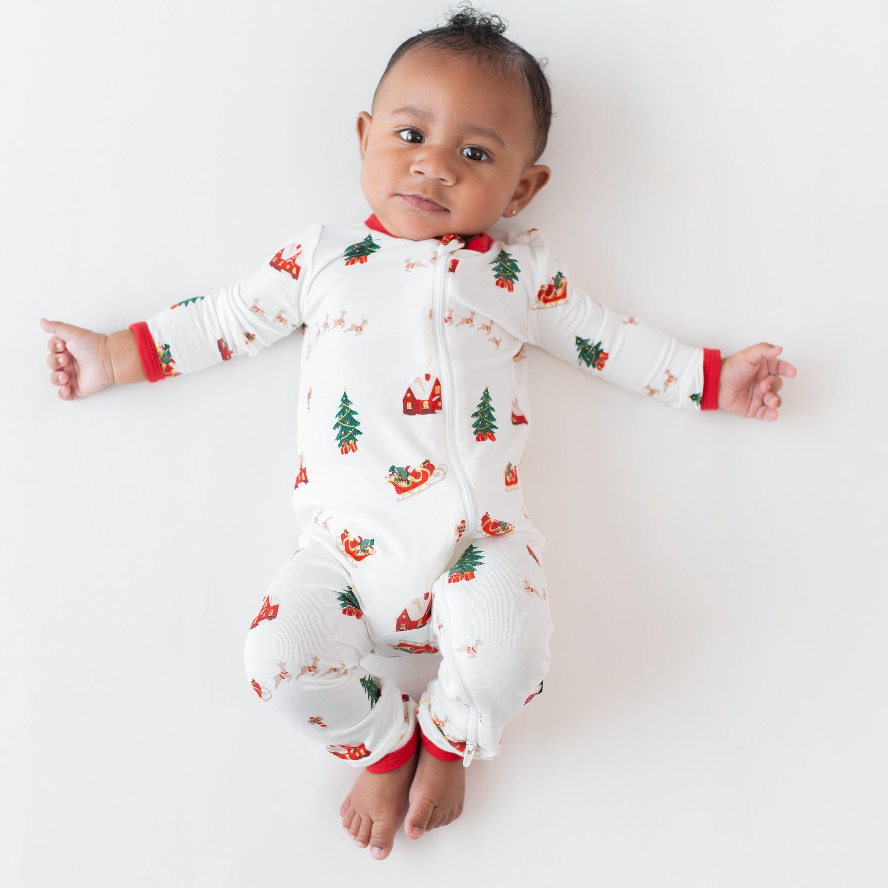 Young infant laying down wearing the Zippered Romper in Santa Sleigh