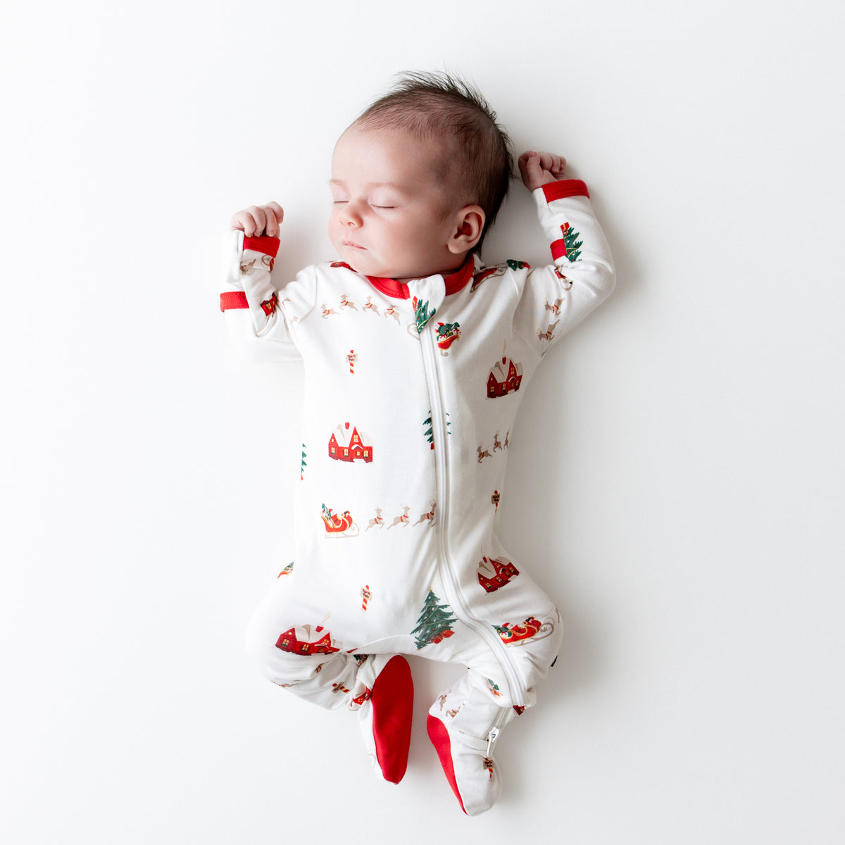 Sleeping newborn wearing the Zippered Footie in Santa Sleigh