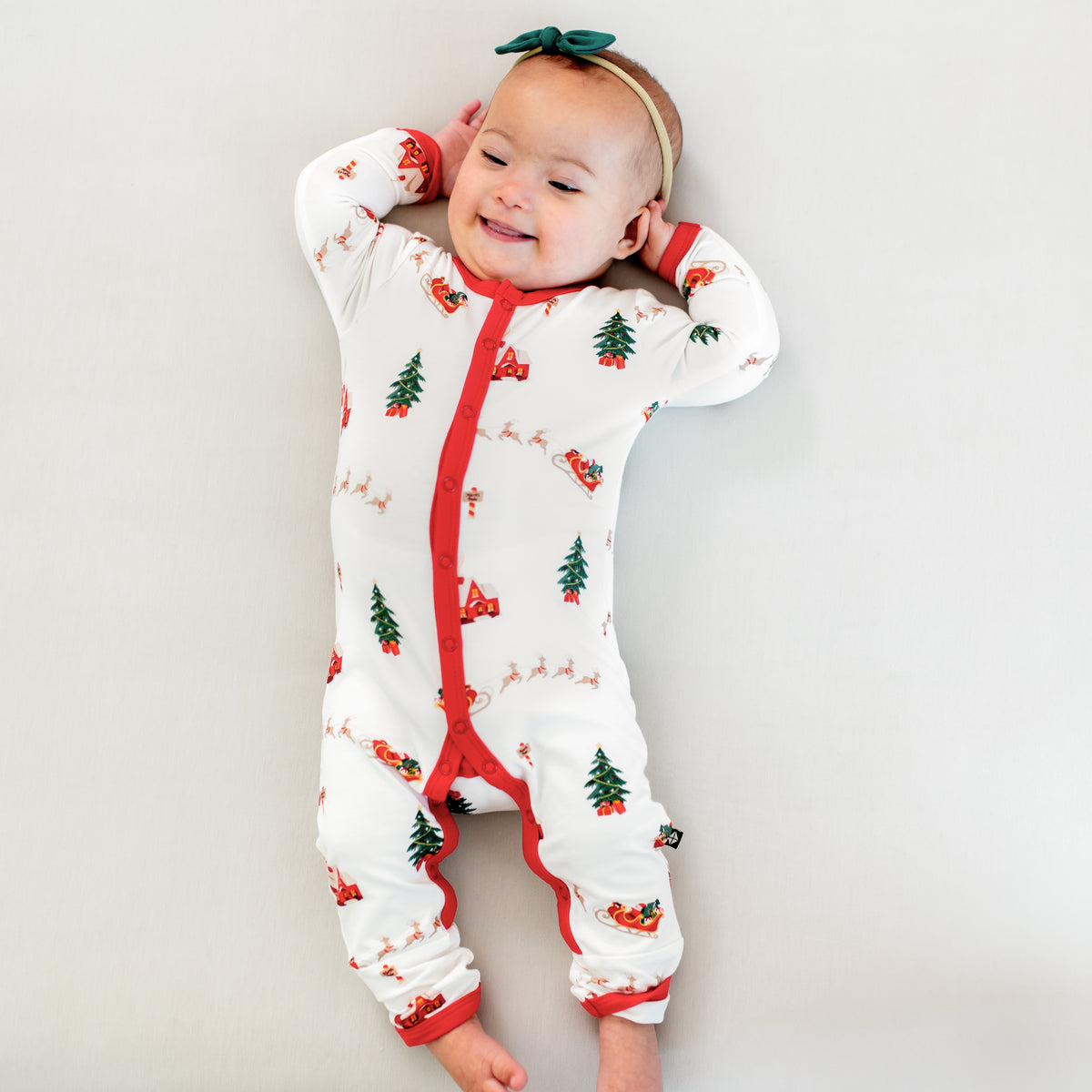 Smiling infant laying down wearing the Romper in Santa Sleigh with a Tiny Nylon bow in emerald