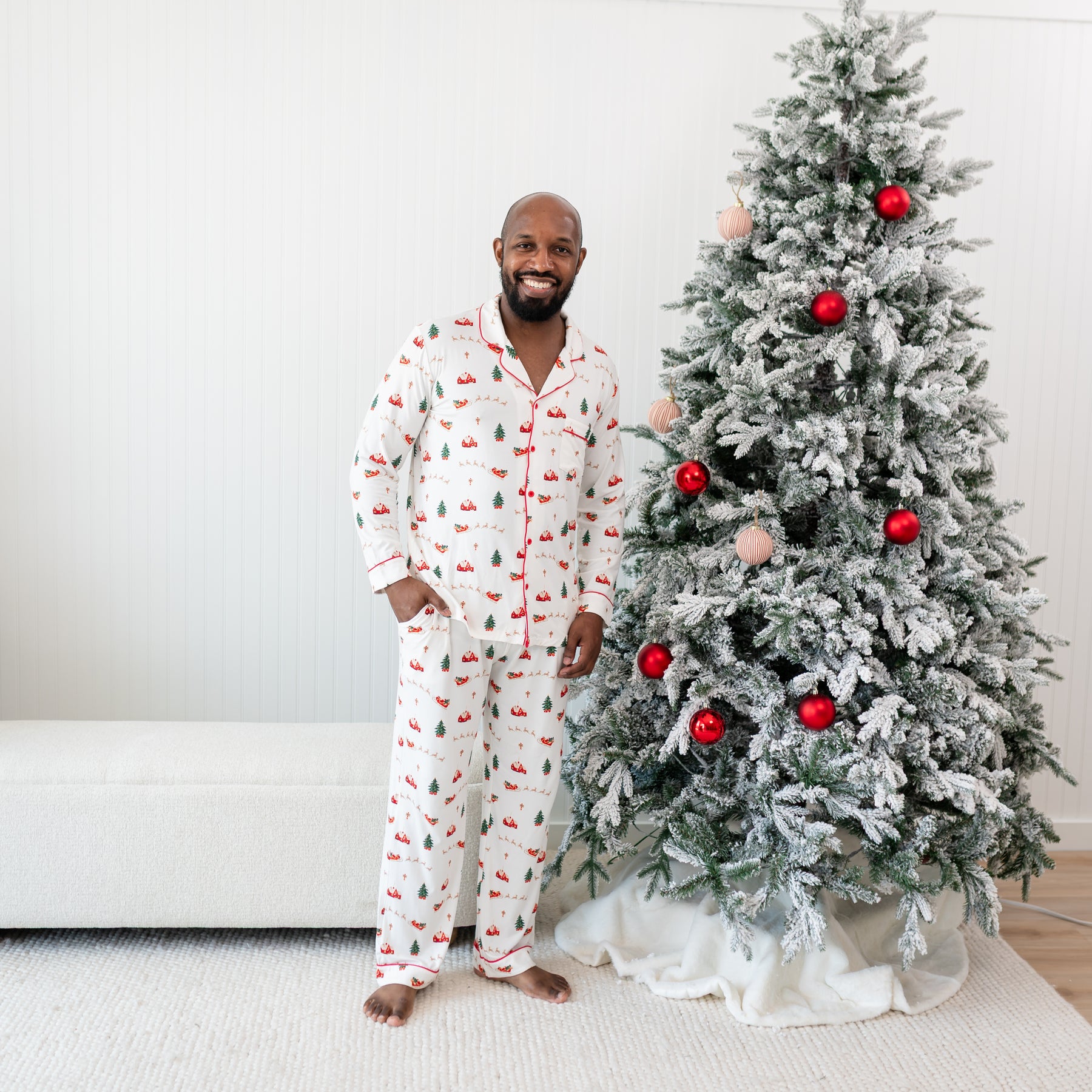 Male model standing beside a Christmas Tree wearing the Men's Long Sleeve Pajama Set in Santa Sleigh