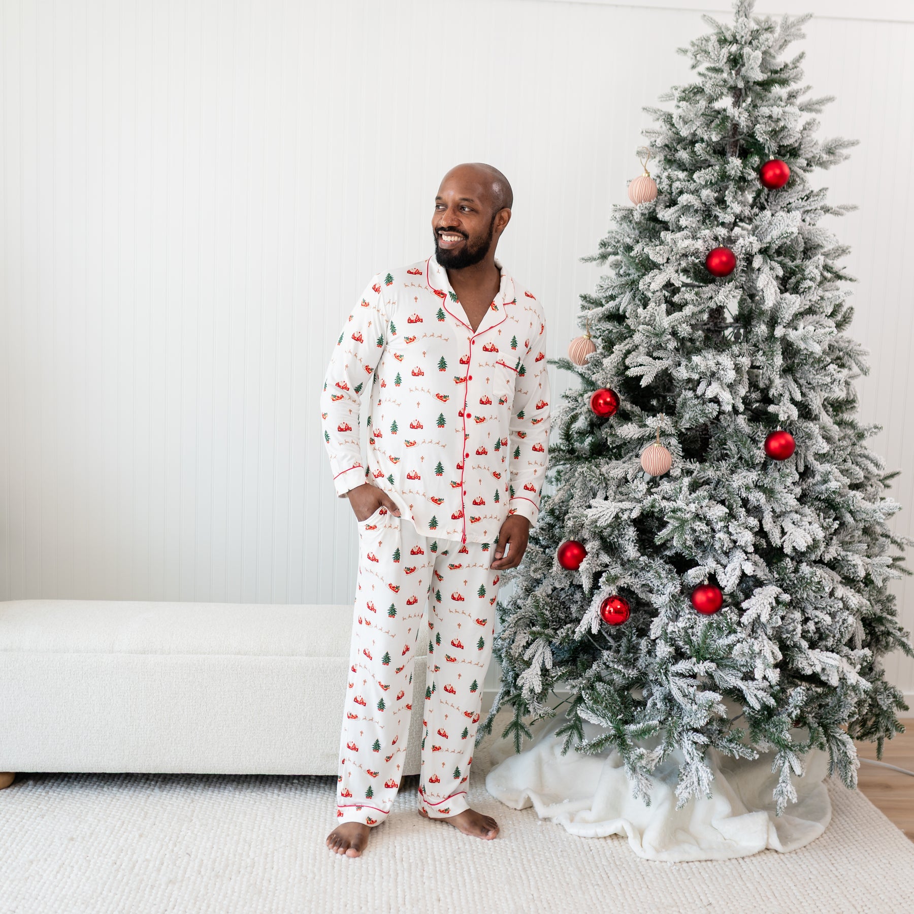 Male model standing beside a Christmas tree looking off to the side wearing the Men's Long Sleeve Pajama Set in Santa Sleigh