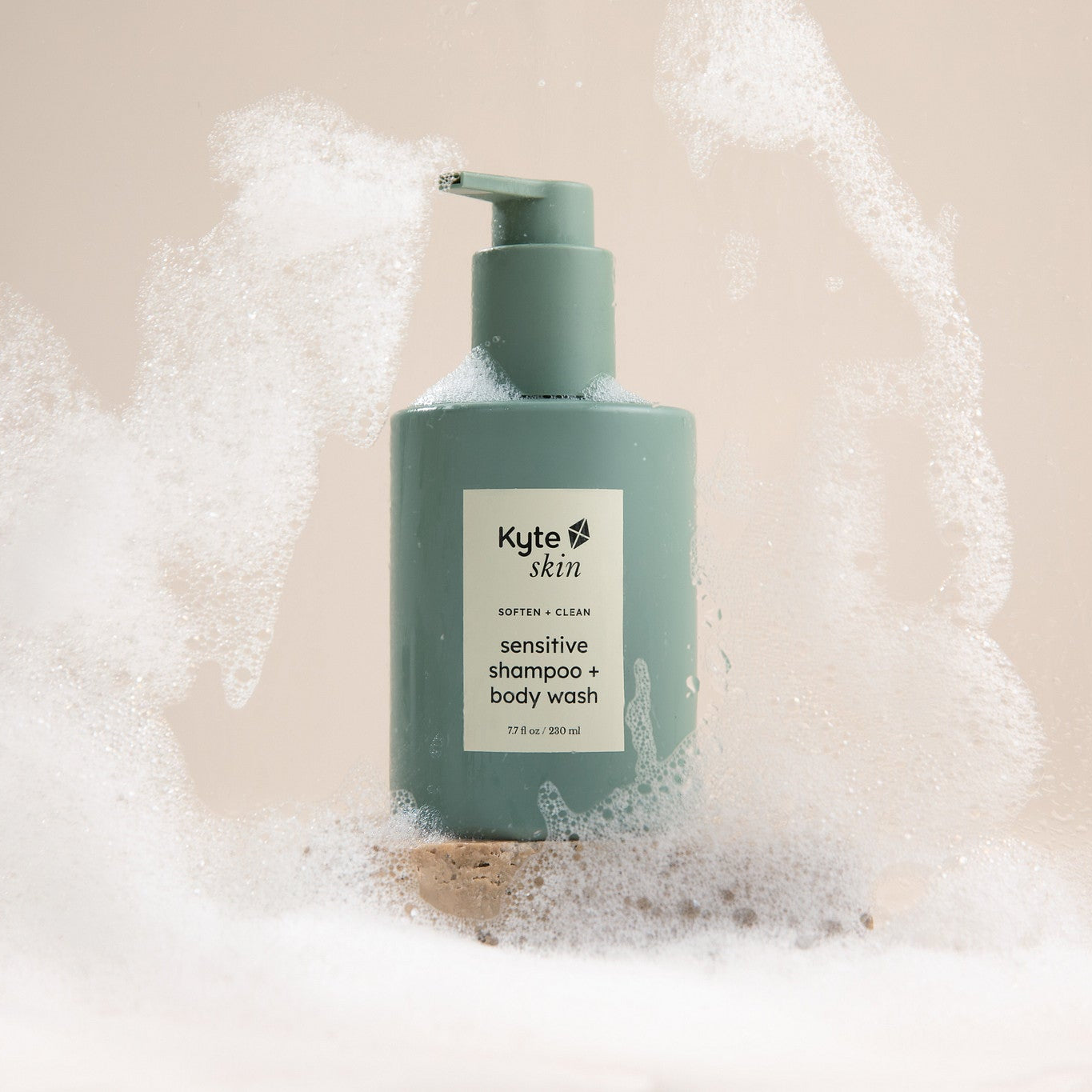 Green bottle of Kyte Skin soap and body wash with bubbles on a beige background