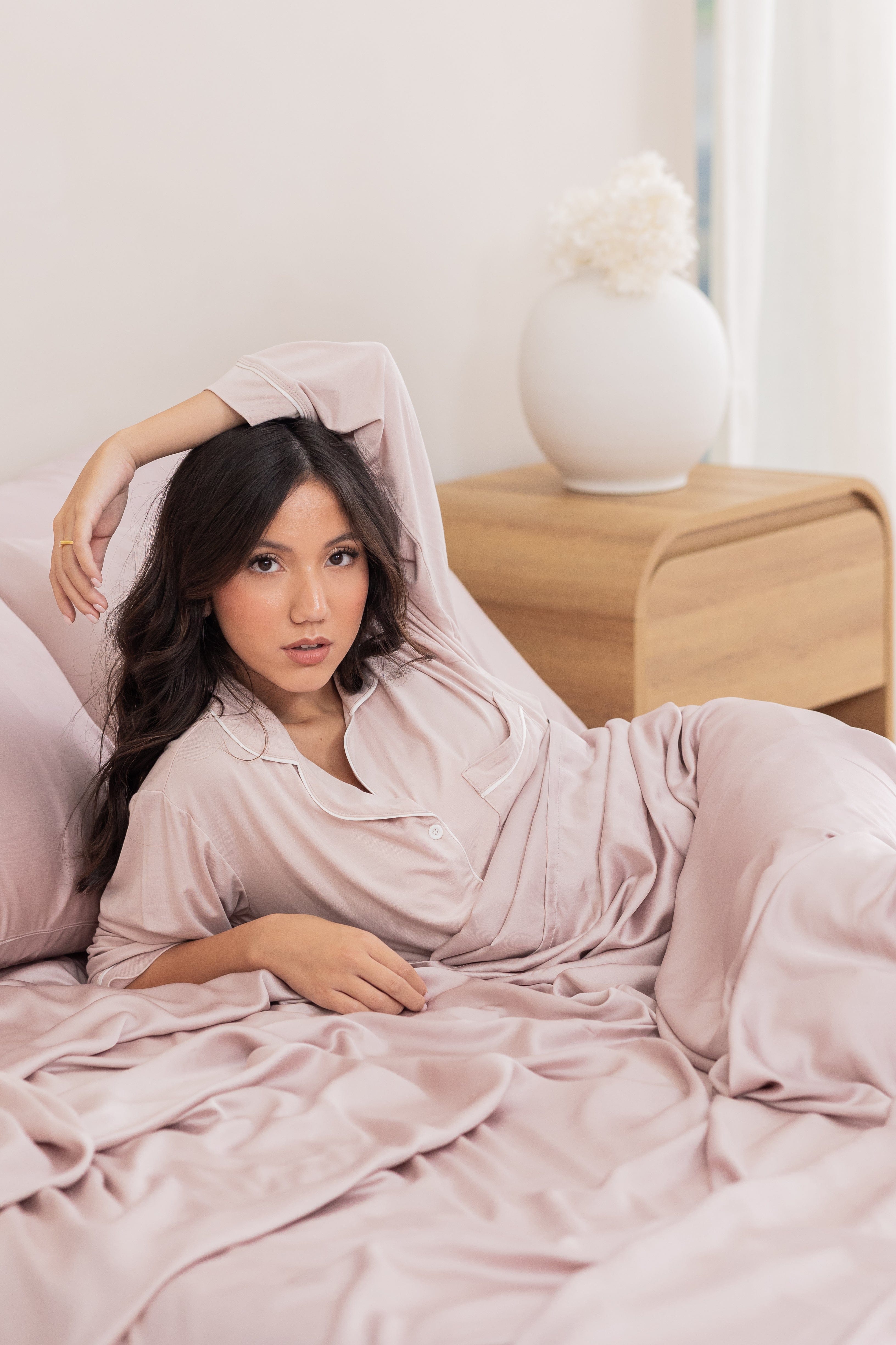 Female laying in bed on the Bamboo Sateen Sheet Set in Rose Quartz with one arm resting over her head