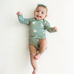 Infant laying on a blanket sticking her tongue out wearing the Long Sleeve Bodysuit in Silly Goose and Ribbed Nylon Tiny Bow in Thyme